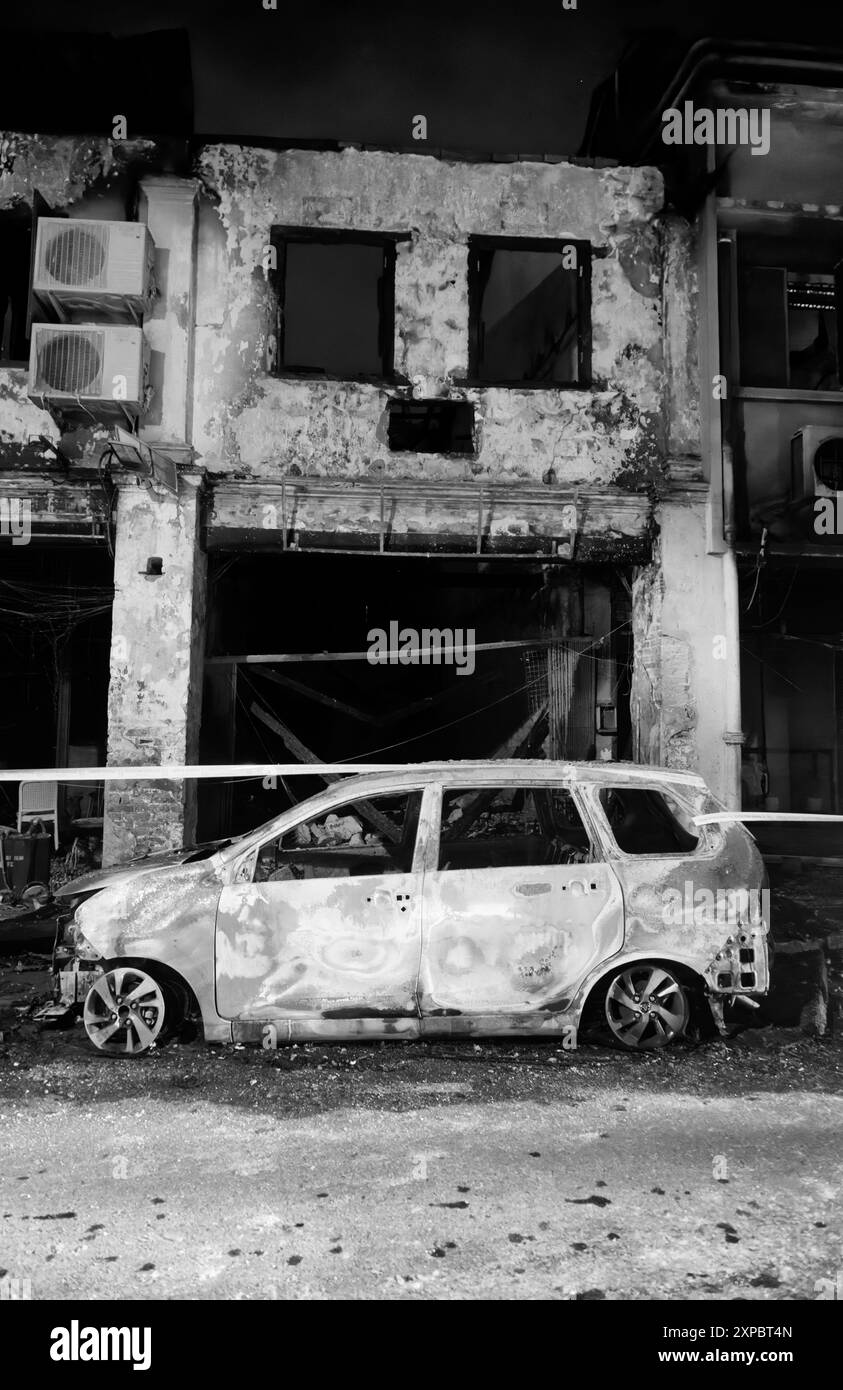 Altes chinesisches Ladenhaus, Feuer beschädigt durch den ausgebrannten Autorahmen davor, Carpenter Street, Kuching, Malaysia schwarz-weiß monochrom Stockfoto