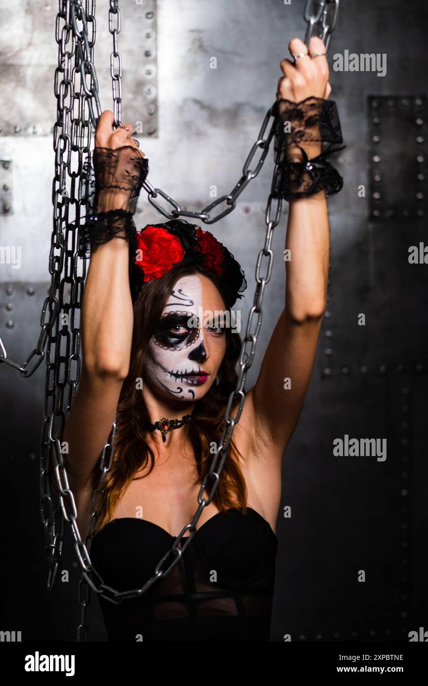 Frau mit Tagesfarbe und Blumenkrone hält Ketten in einer gotischen, industriellen Umgebung. Stockfoto