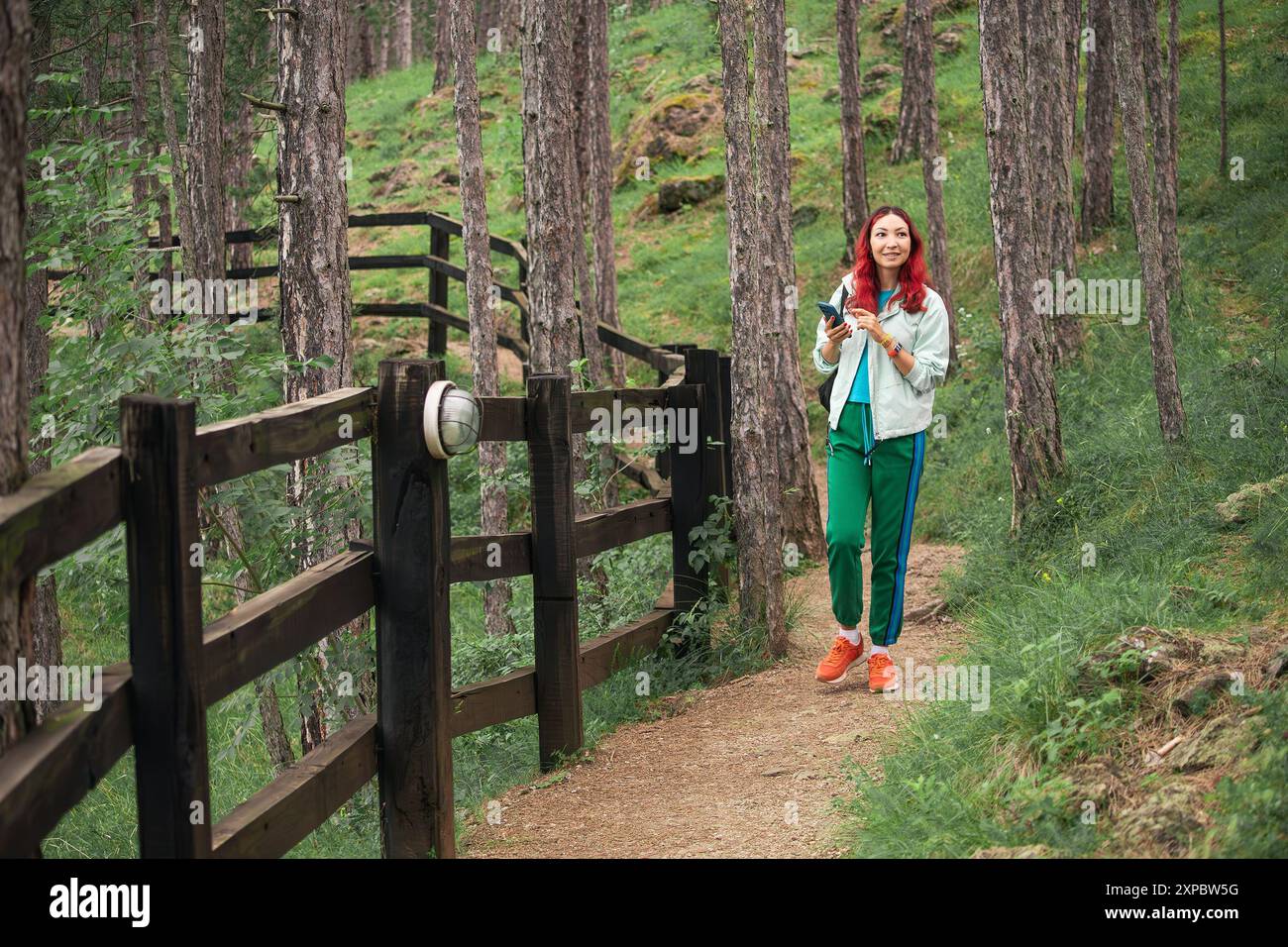 Eine Frau, die auf einem Waldweg wandert, umgeben von üppig grünen Bäumen, mit Rucksack und einem Gefühl für Abenteuer. Stockfoto