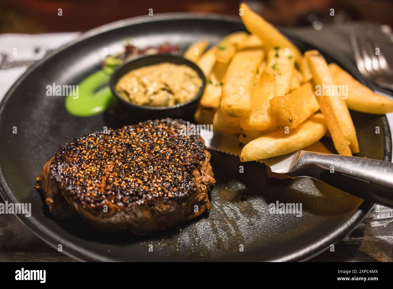 Gegrilltes Rindersteak mit schwarzem Pfeffer, Pommes frites, Gemüse auf Keramikplatte auf dem Tisch Stockfoto