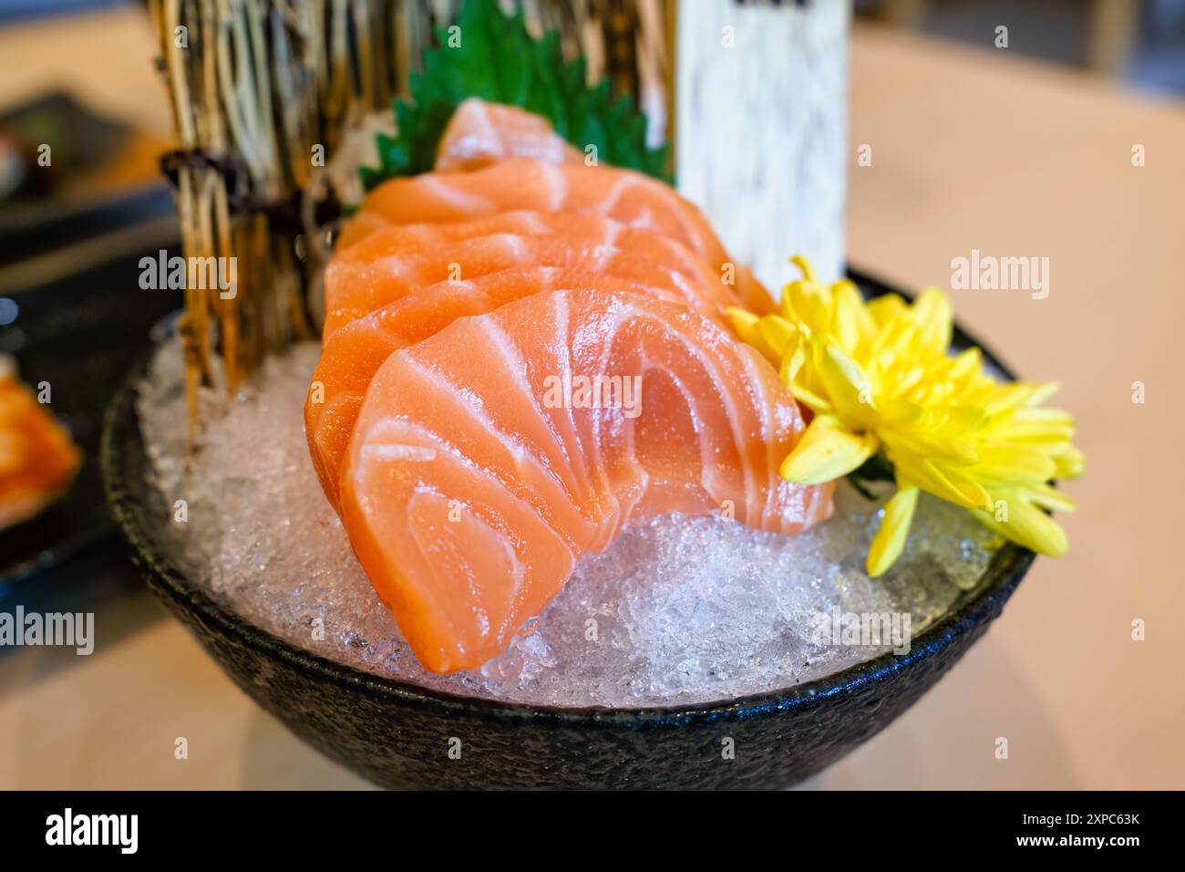 Keramikschale mit in Scheiben geschnittenem frischem Lachs-Sushi mit gelben Blüten auf zerstoßenem Eis im japanischen Restaurant Stockfoto