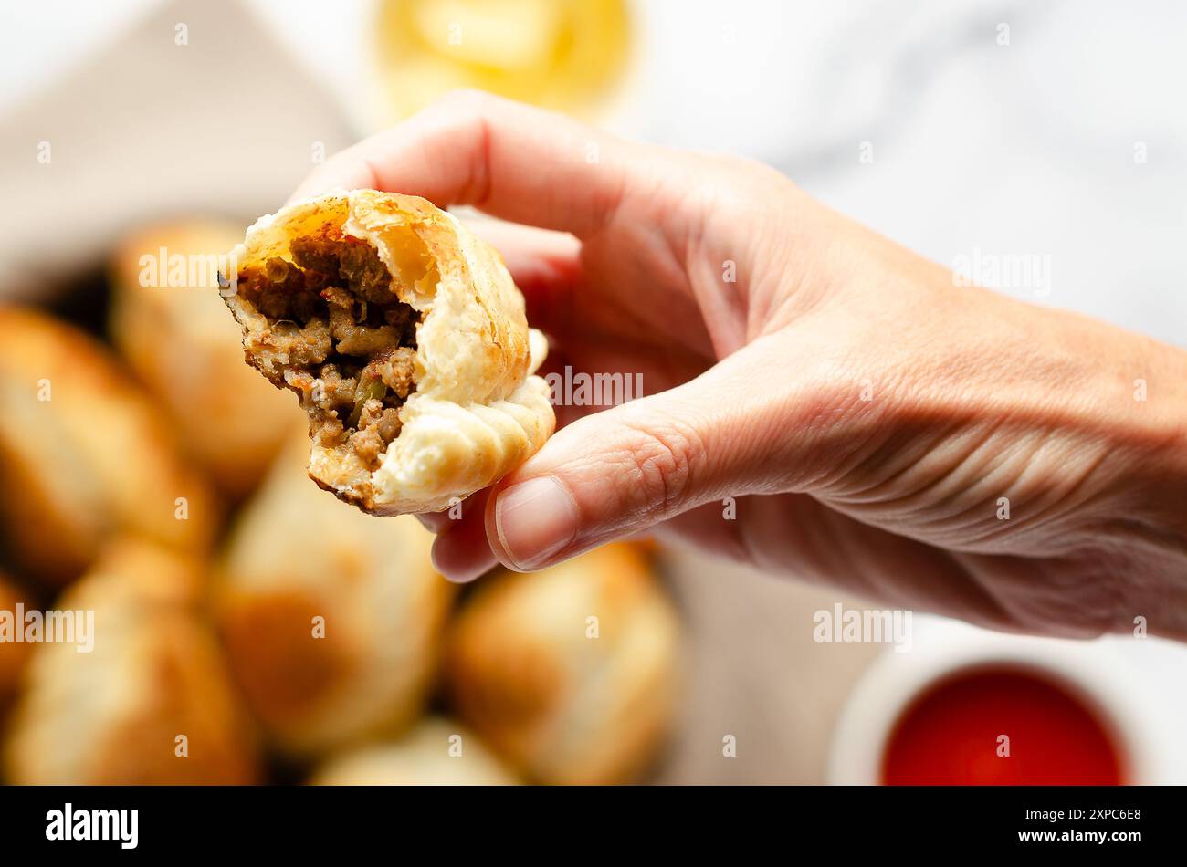 Eine weibliche Hand, die eine gebissene argentinische Rinderempanada hält. Stockfoto