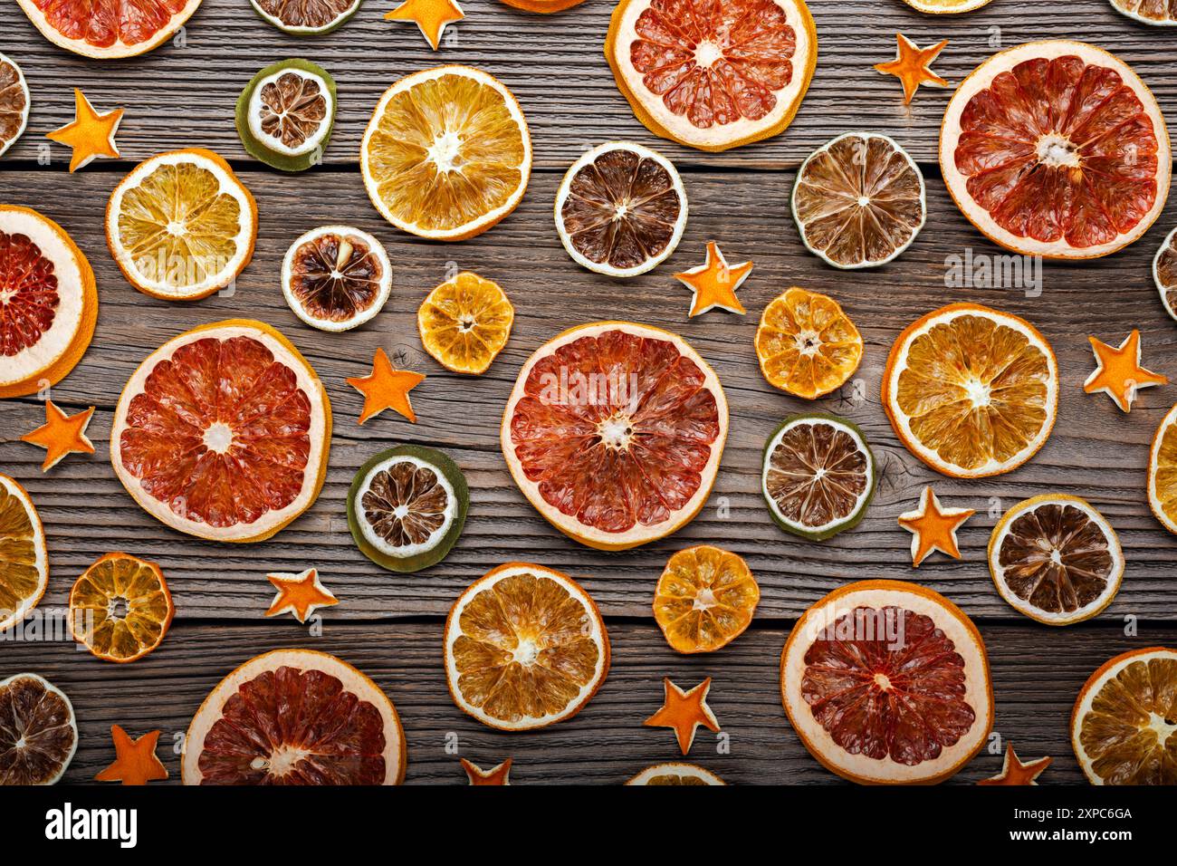 Getrocknete Orangen-, Grapefruit-, Zitronen- und Limettenscheiben mit Orangenschalen-Sternen auf rustikalem Holzbrett. Weihnachten oder Neujahr Ornament Border Hintergrund Stockfoto