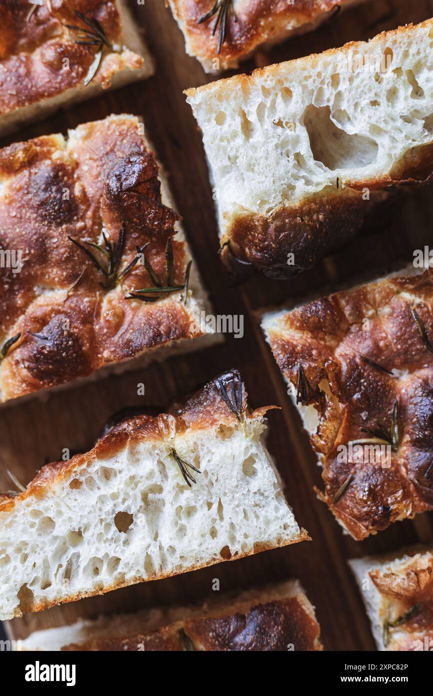 Detaillierte Nahaufnahme von geschnittenen Focaccia-Brotstücken auf einer Holzoberfläche, die die luftige Textur und die knackige, goldbraune Kruste des Brotes zeigt. Ro-Zweige Stockfoto