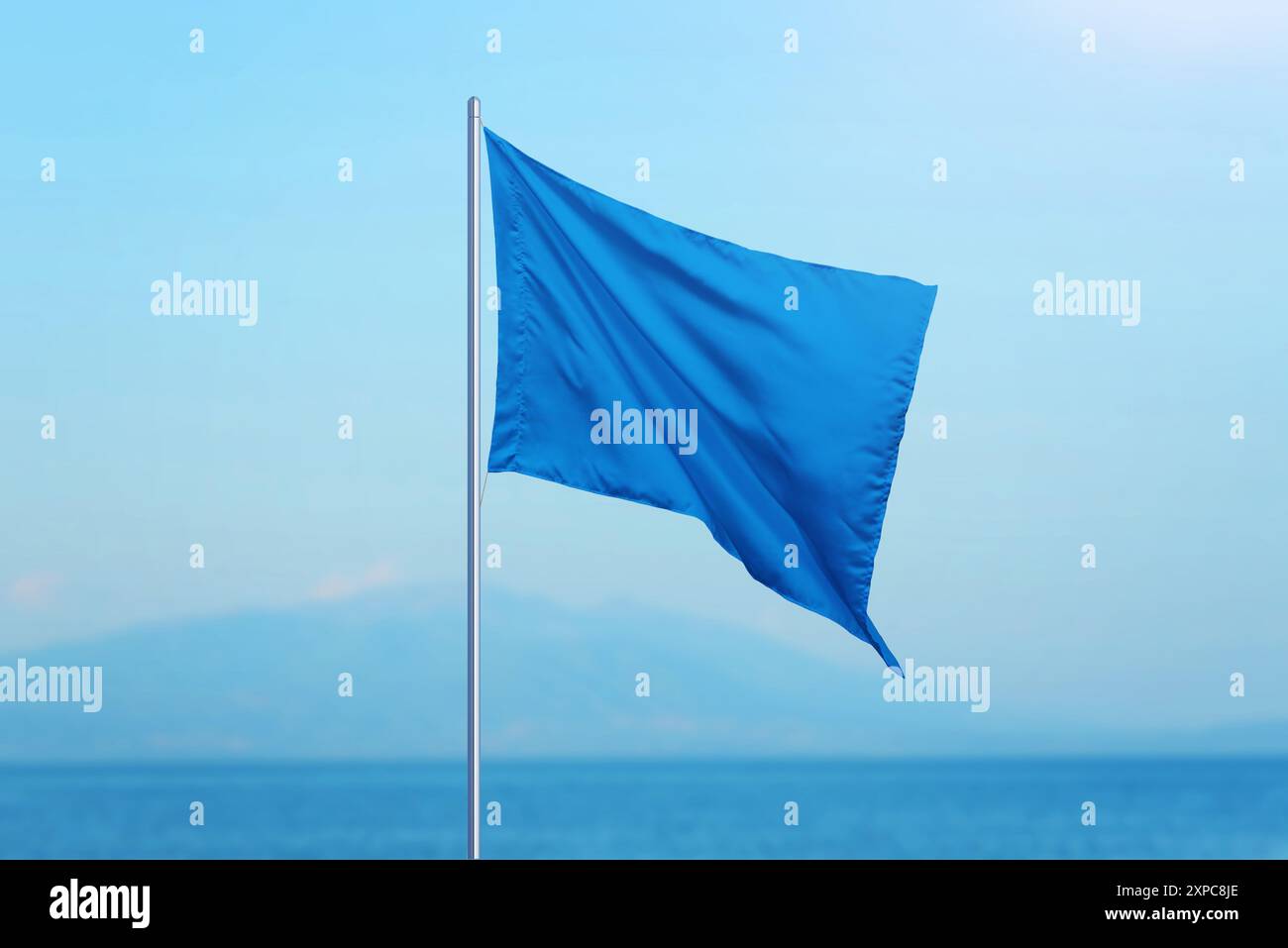 Blaue Flagge mit dem Meer im Hintergrund. Strände, die hohen Standards entsprechen, sind mit einer blauen Flagge markiert, die Qualität und Sicherheit symbolisiert. Ideal für Reisen Stockfoto