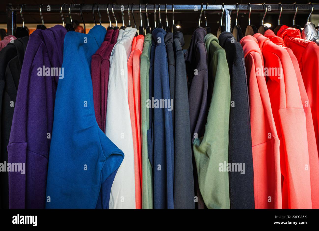 Ein lebhaftes Sortiment an Hoodies hängt ordentlich auf einem Regal in einem Einzelhandelsgeschäft und zeigt verschiedene Farben und Styles, die Kunden zum Durchstöbern bringen. Stockfoto