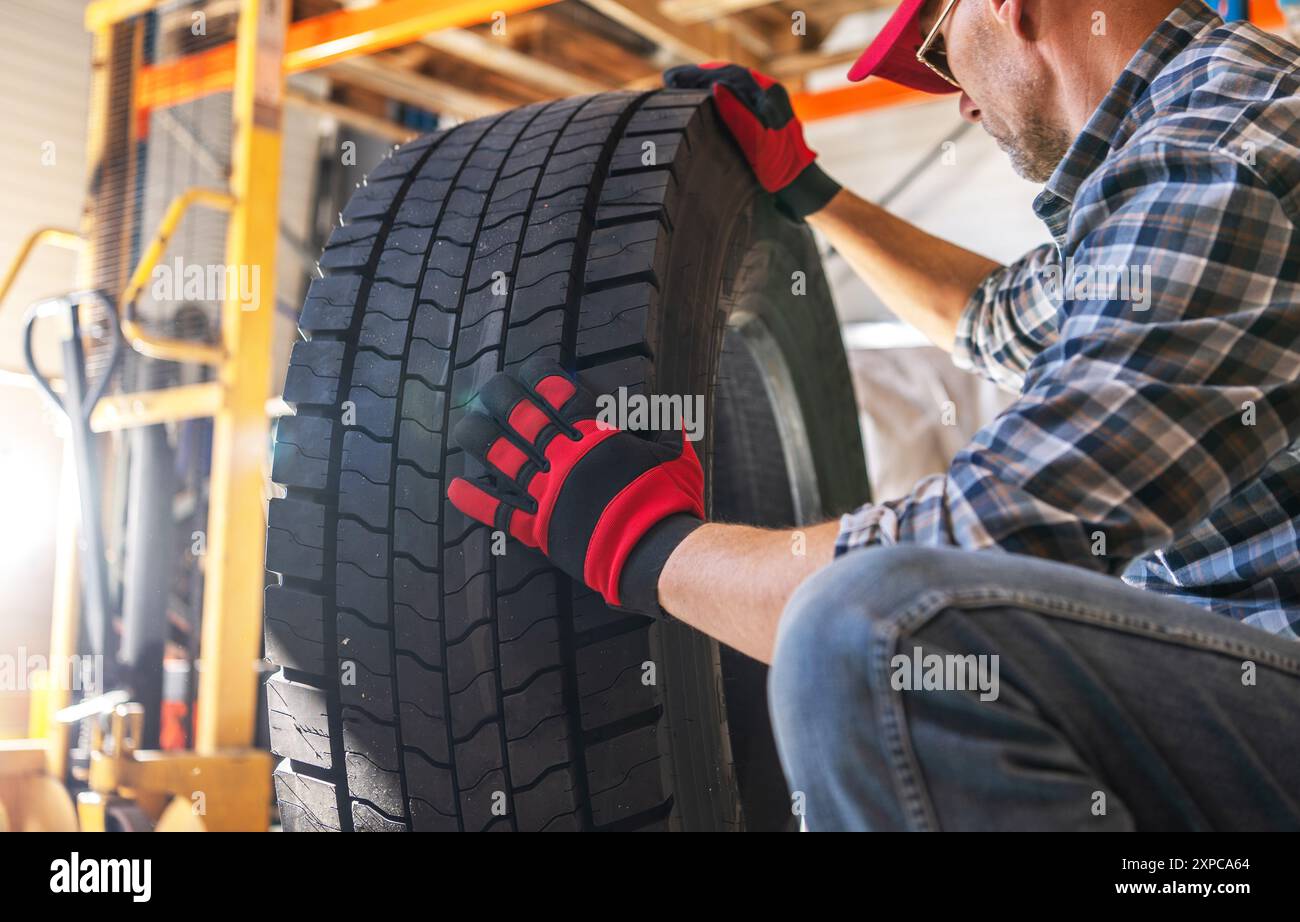 Eine Person mit Handschuhen untersucht einen großen Lkw-Reifen in einer Werkstatt, wobei Werkzeuge und Ausrüstung im Hintergrund sichtbar sind. Stockfoto
