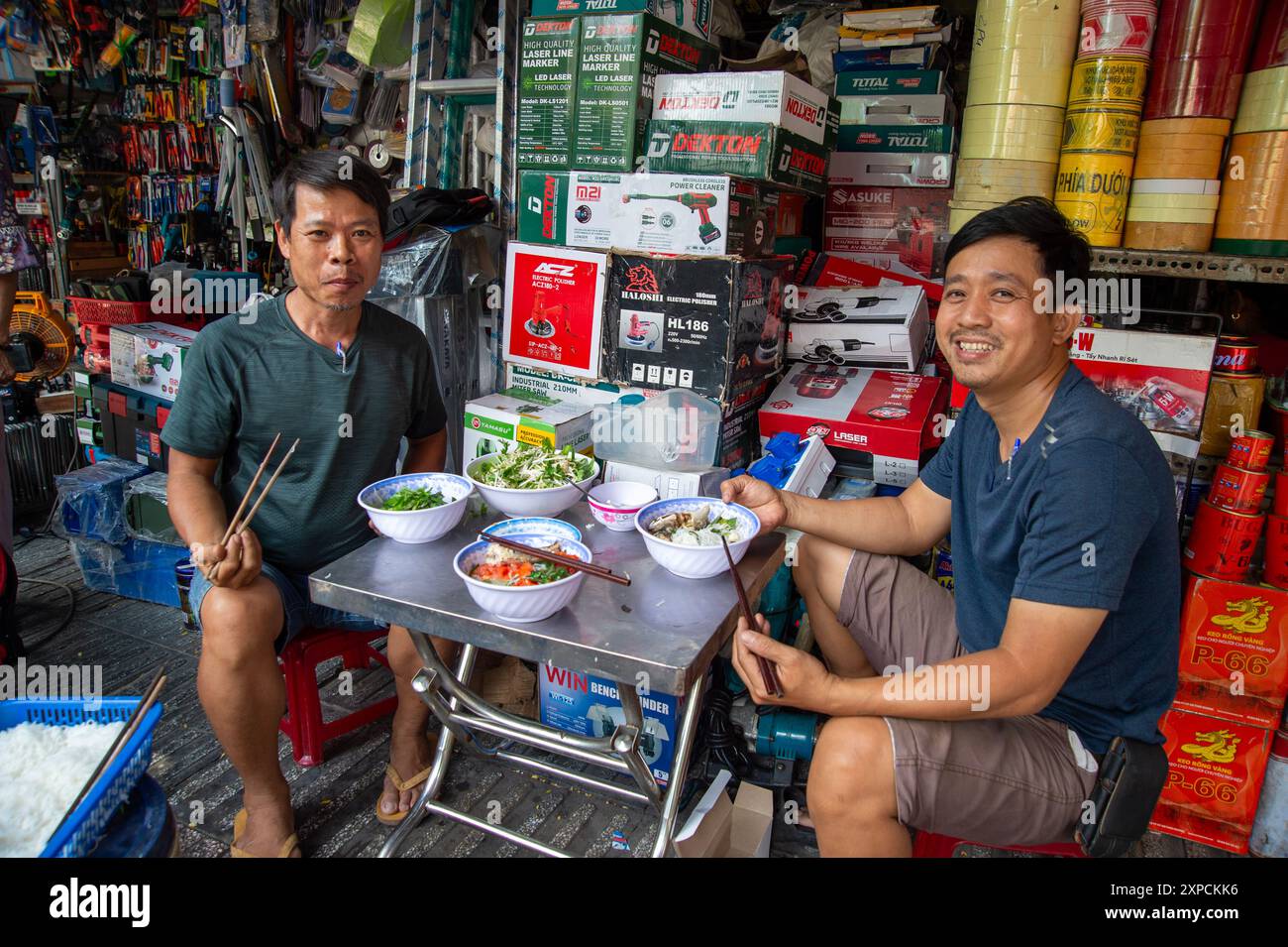 Zwei lächelnde vietnamesische Ladenarbeiter sitzen mittags im Stadtteil pham ngu lao in Saigon Vietnam in Schüsseln mit vietnamesischem Essen Stockfoto