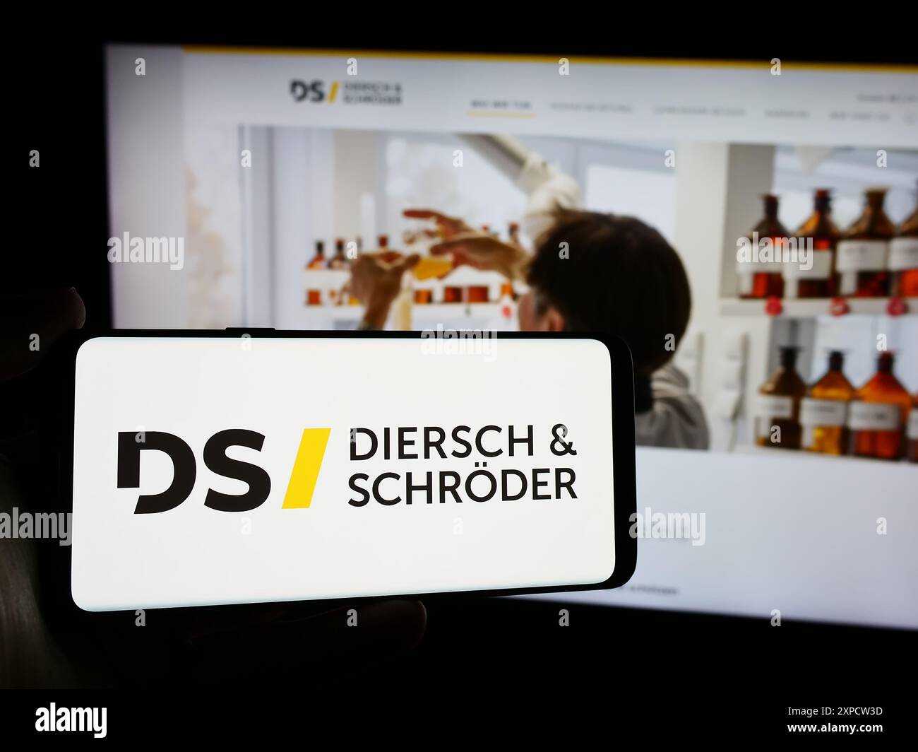 Person mit Mobiltelefon mit Logo der deutschen Firma Diersch and Schröder GmbH Co. KG vor der Business-Webseite. Schwerpunkt auf dem Display des Telefons. Stockfoto