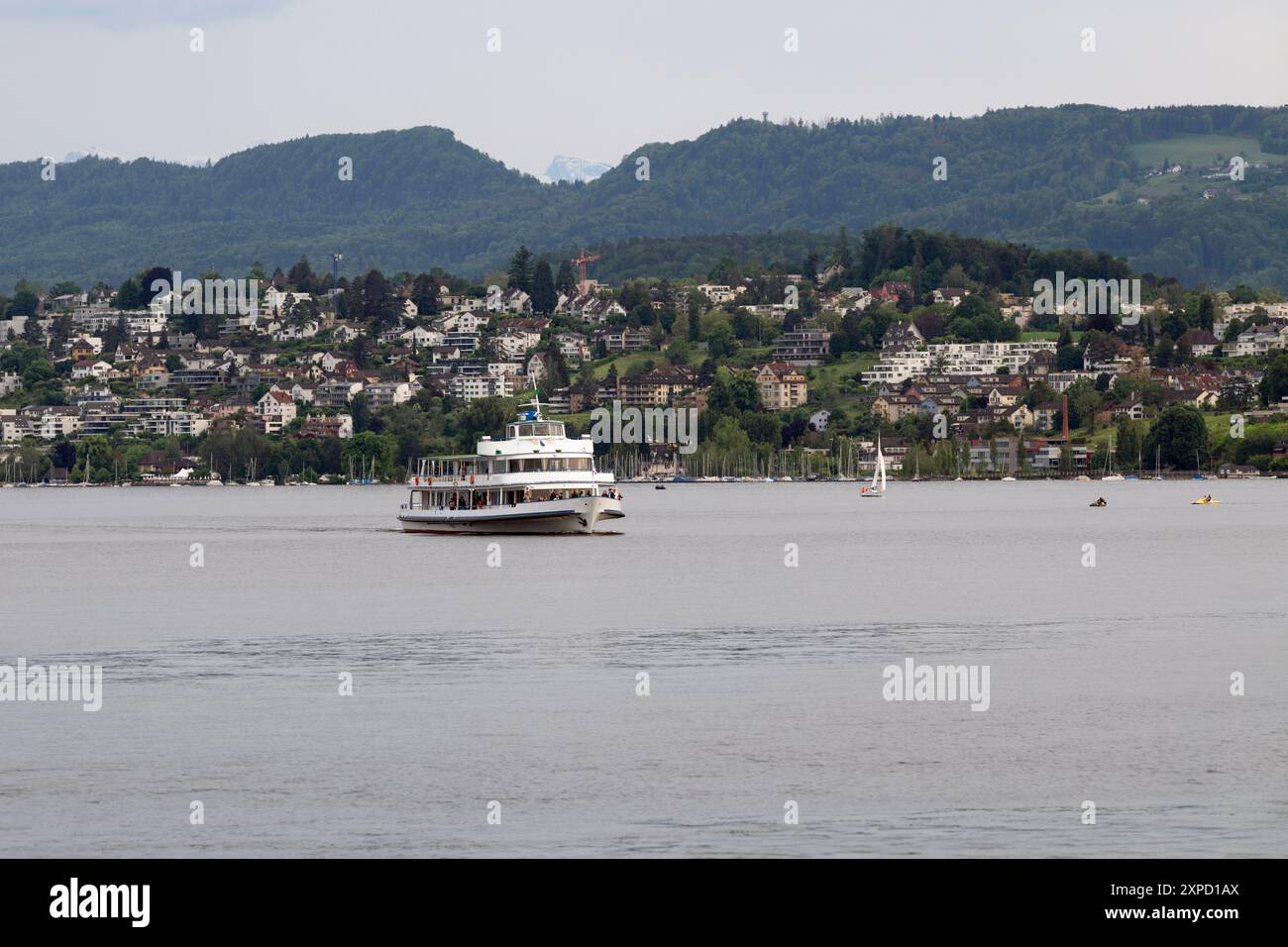 Sightseeing-Boot fährt durch den See mit einer Stadt und Seehafen, die sich über Hügel im Hintergrund ausbreitet Stockfoto