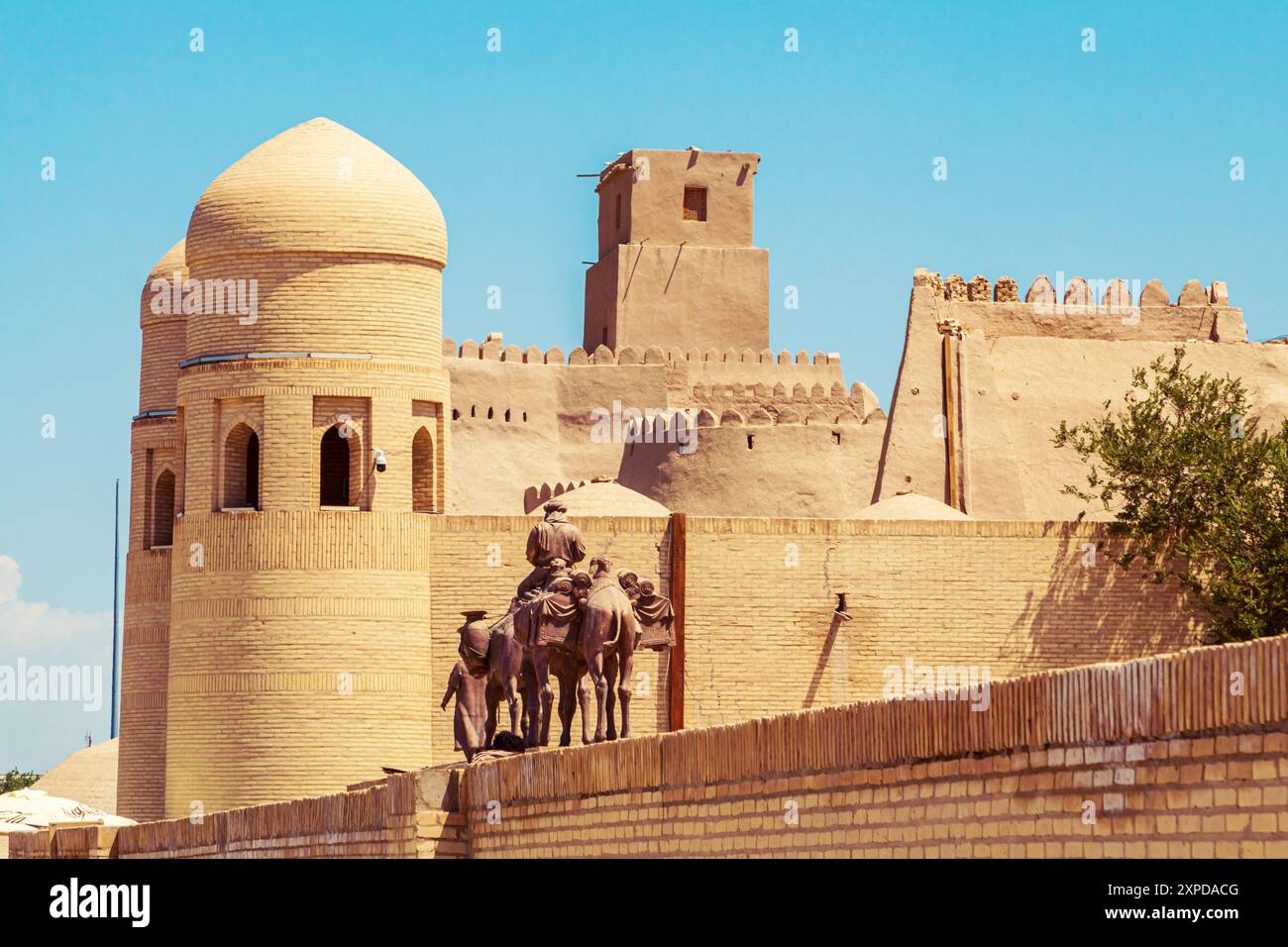 Skulpturengruppe einer Karawane mit Kamelen, die Güter entlang der Seidenstraße in der Nähe der alten Stadtmauern transportieren. Chiwa, Usbekistan - 17. Juli 2024. Stockfoto