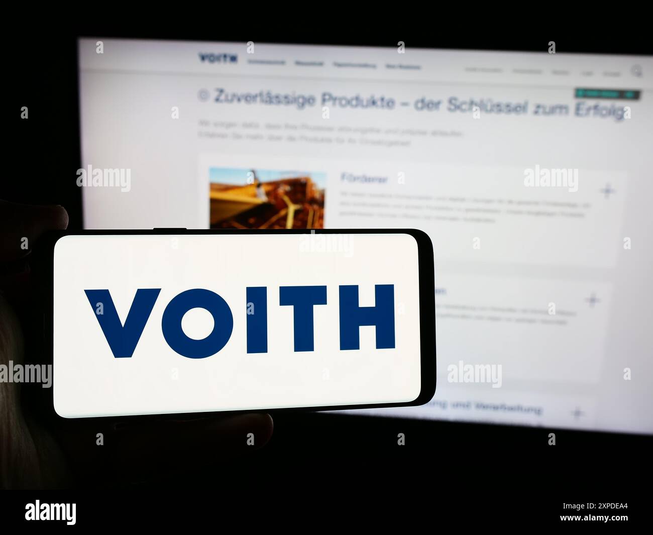 Person mit Smartphone und Logo des deutschen Technologieunternehmens Voith GmbH Co. KGaA vor der Website. Schwerpunkt auf dem Display des Telefons. Stockfoto