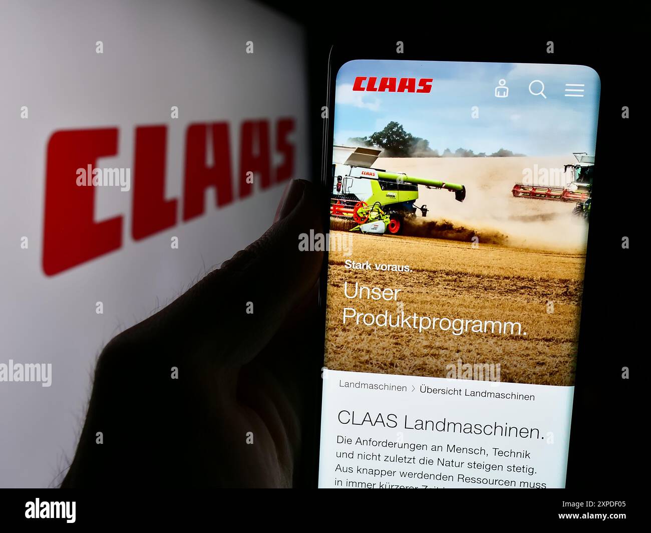 Person mit Handy mit Webseite des deutschen Landmaschinenunternehmens Claas KGaA mbH vor Logo. Konzentrieren Sie sich auf die Mitte des Telefondisplays. Stockfoto