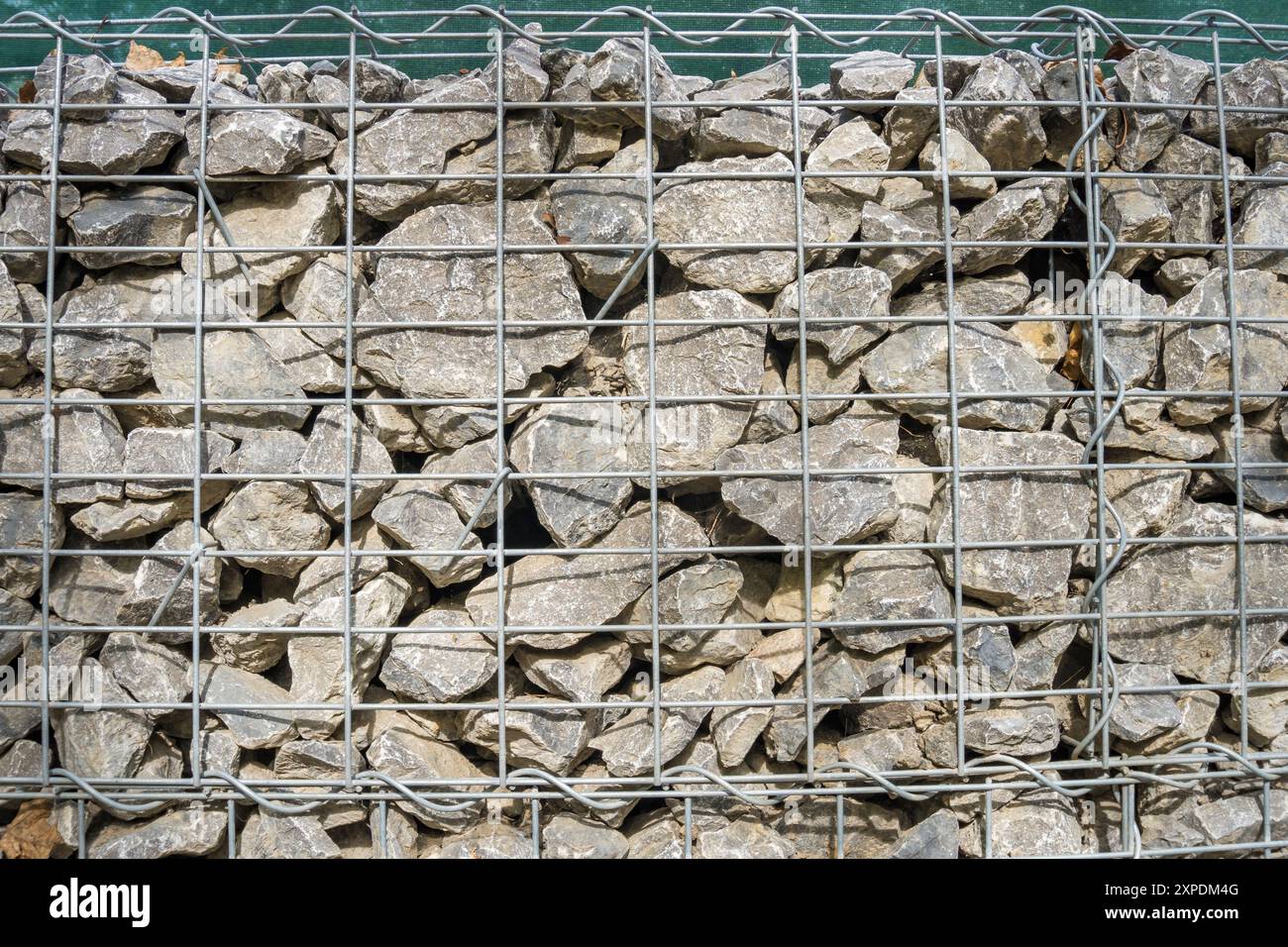 Gabion, ein Zaun aus Meeressteinen und großem blauem Glas in einer Maschenöffnung. Stockfoto