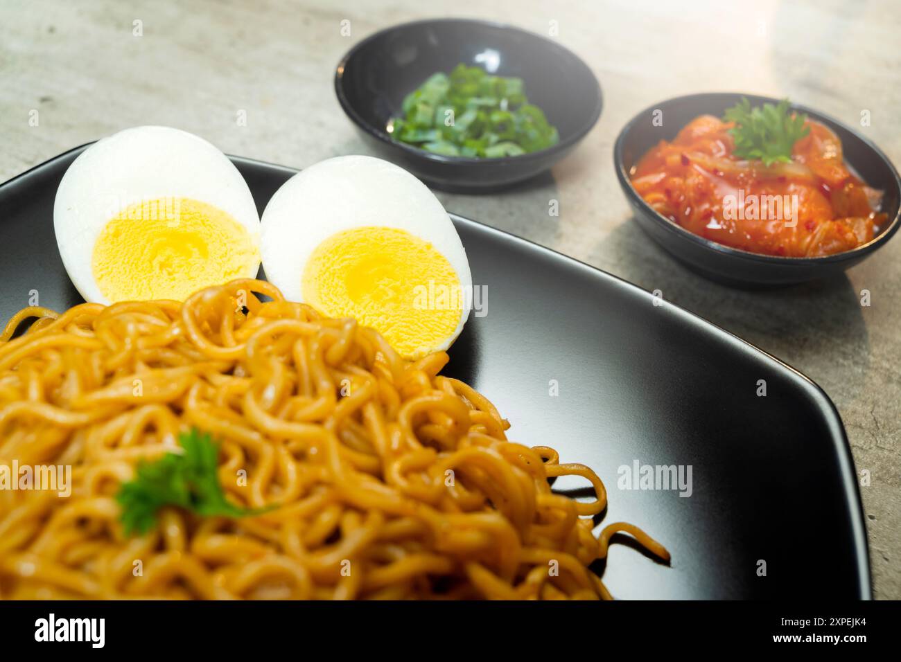 Ein Teller mit Instantnudeln mit Tomaten und Ei darauf. Der Teller wird auf einen Tisch mit Essstäbchen und Schüsseln gestellt Stockfoto