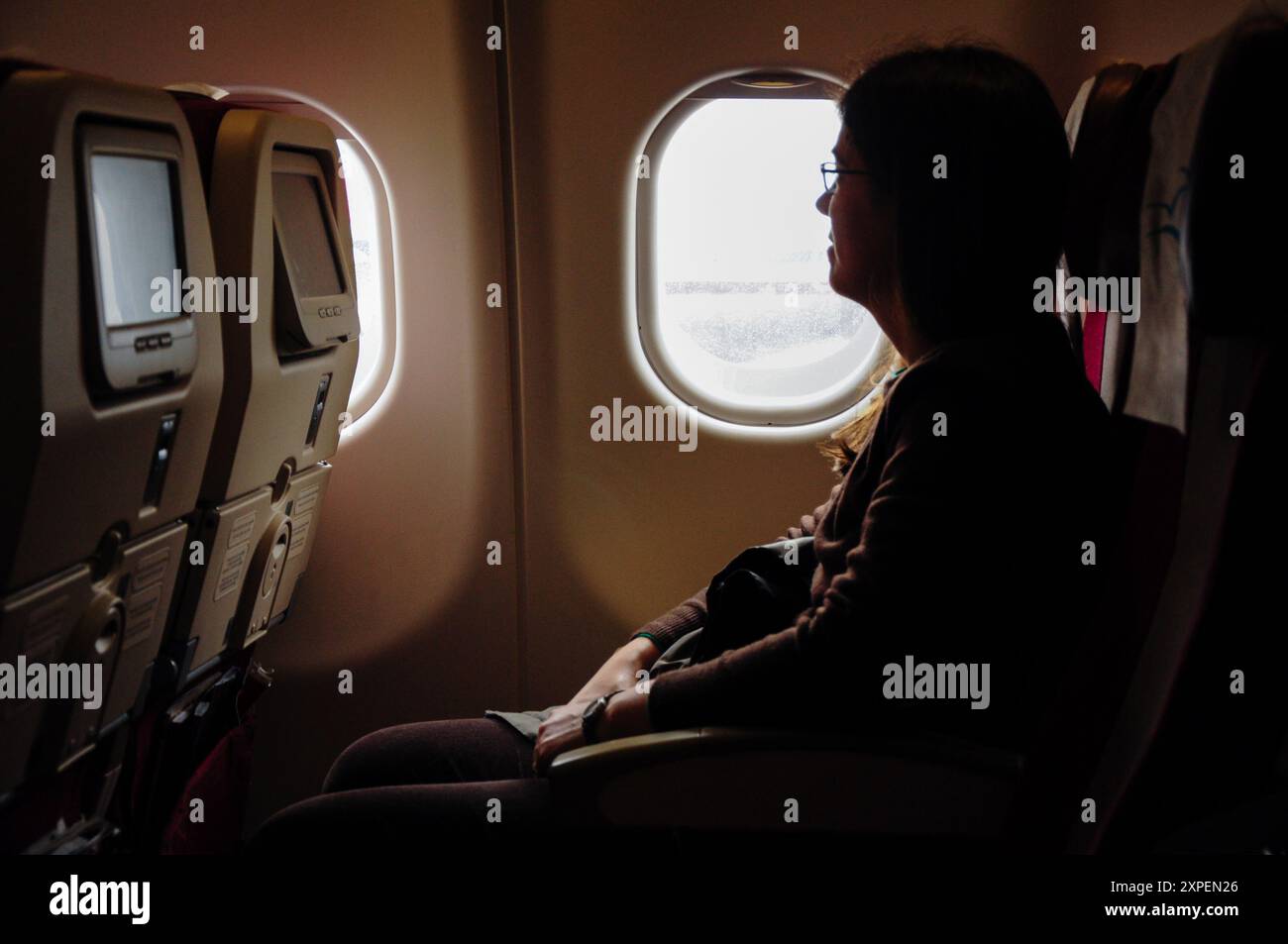 Frau auf einem internationalen Flug, die auf einem Flugzeugsitz am Fenster sitzt. Stockfoto