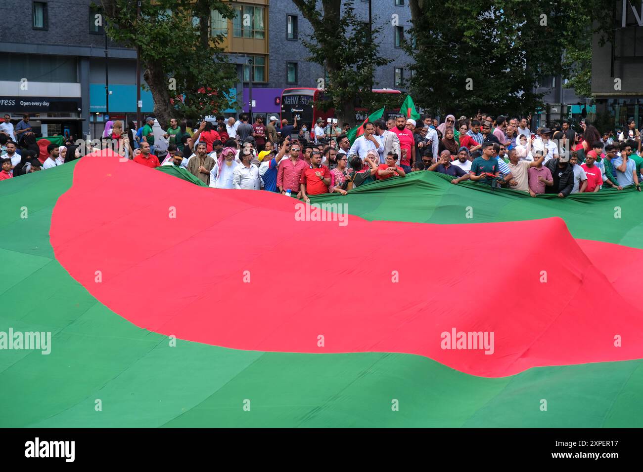 London, UK, 5. August 2024. Die britisch-bangladeschische Gemeinde feierte die Nachricht vom Rücktritt von Premierminister Sheikh Hasina im Altab Ali Park im Osten Londons. Menschenmassen umgeben eine riesige Nationalflagge von Bangladesch. Studentenproteste im südasiatischen Land wegen der Beschäftigungsquoten für die am Befreiungskrieg von 1971 teilnehmenden Beamten führten zu einer zunehmenden Desatisierung der Führung von Frau Hasina. Quelle: Eleventh Photography/Alamy Live News Stockfoto