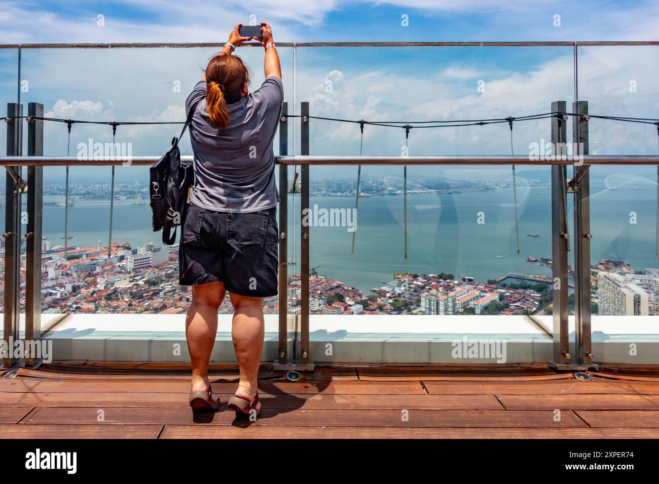 Eine Dame, die auf Zehenspitzen steht und sich ausdehnt, um ein Foto über eine Barriere zu machen, mit ihrem Handy auf der Spitze, Komtar Tower, George Town, Penang, Malaysia Stockfoto