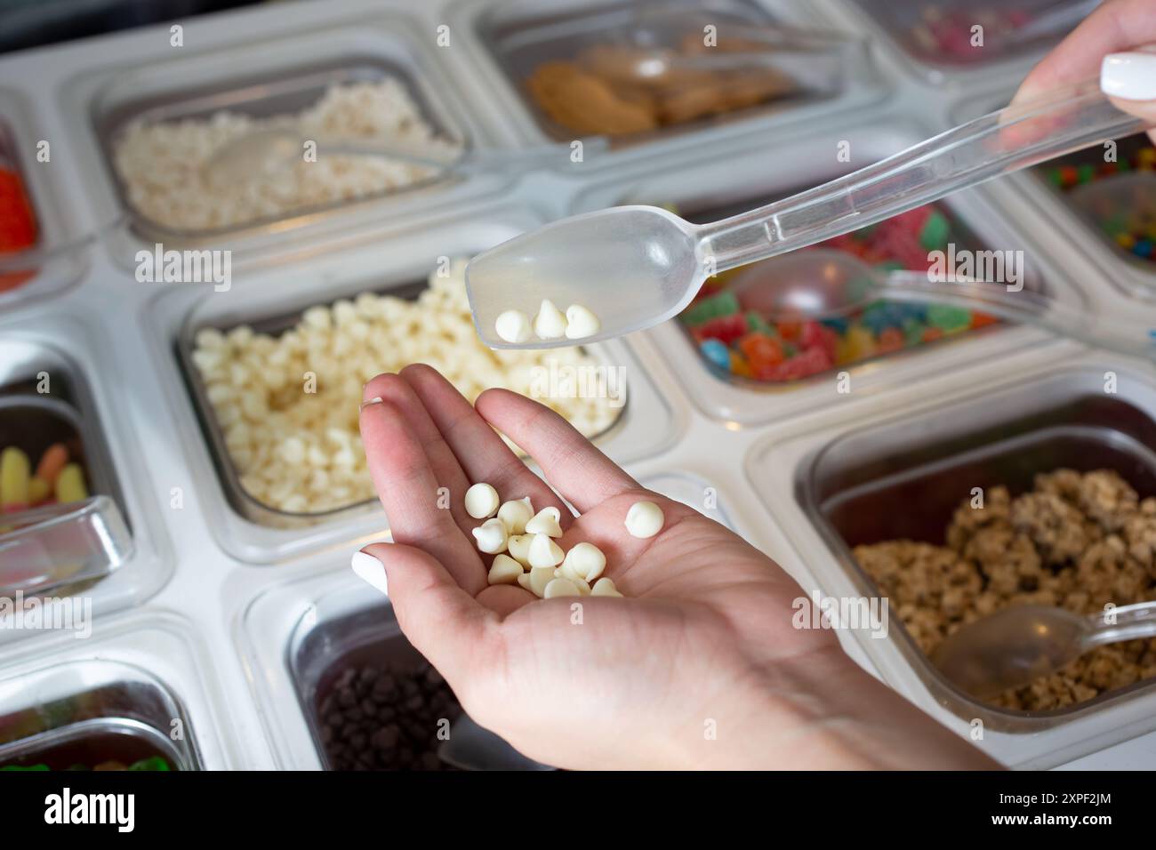 Ein Blick auf eine Hand, die über einer Theke voller verschiedener Beläge steht, die in einem lokalen Tiefkühljoghurt-Restaurant zu sehen ist. Stockfoto
