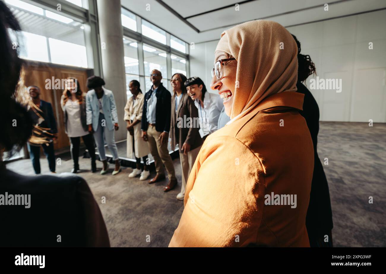 Ein vielfältiges Team engagiert sich in einer Bindungsaktivität, wobei eine muslimische Frau während eines Workshops im Kreis lacht. Stockfoto