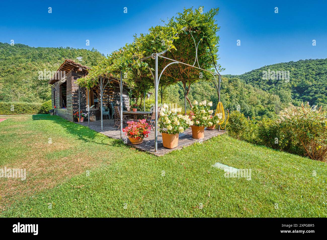 Ein ruhiger Rückzugsort auf der Landschaft: Eine bezaubernde Pergola mit üppigem Grün und leuchtenden Blumen vor dem Hintergrund sanfter Hügel Stockfoto
