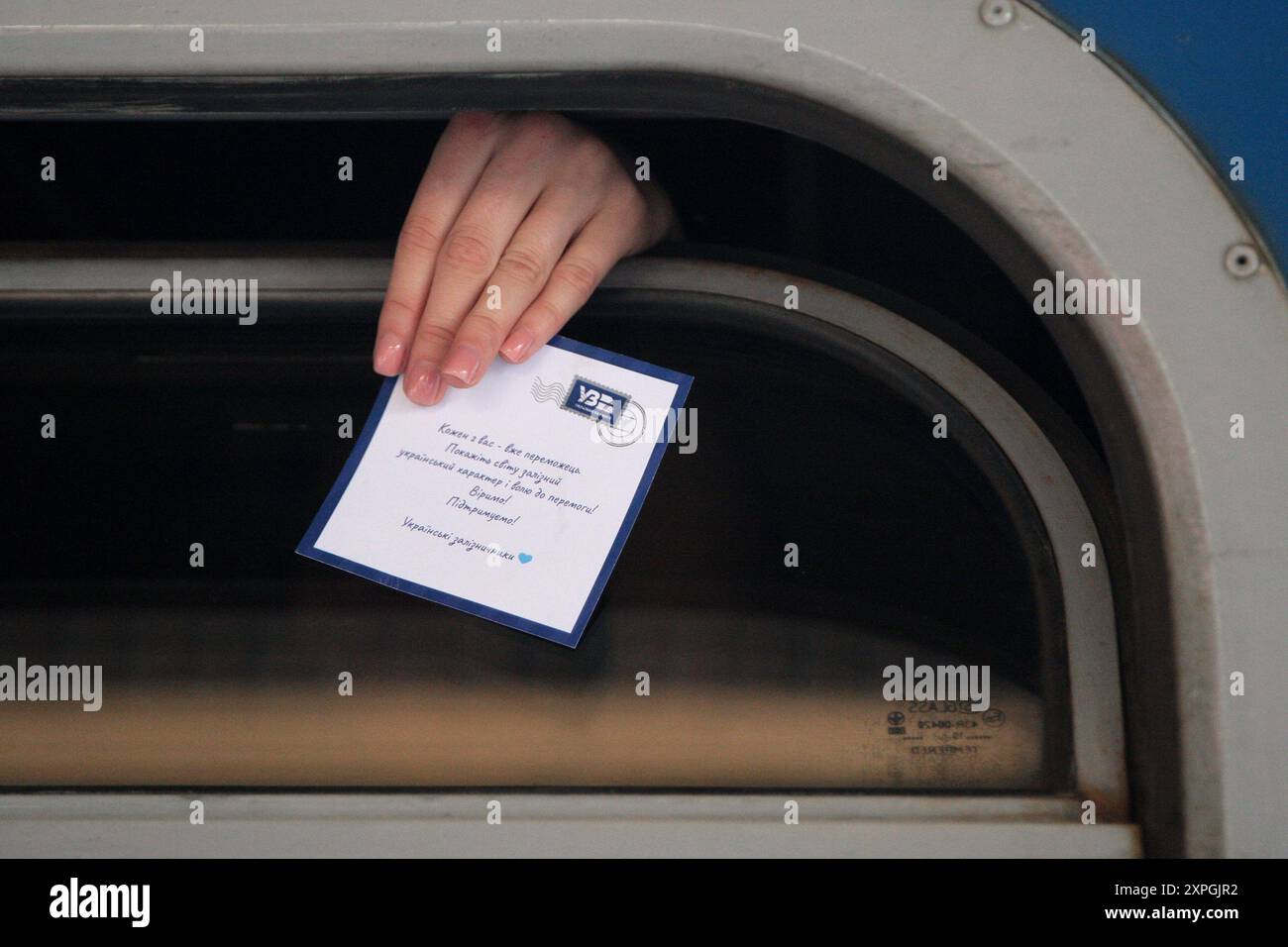 KIEW, UKRAINE - 2. AUGUST 2024 - Eine Frau zeigt eine Postkarte, die Glück wünscht, in einem Zugfenster, während das ukrainische Freistil-Wrestling-Team der Frauen vom Bahnhof Kiew-Pasazhyrskyi zu den Olympischen Spielen 2024 in Kiew, Hauptstadt der Ukraine, abfährt. Stockfoto