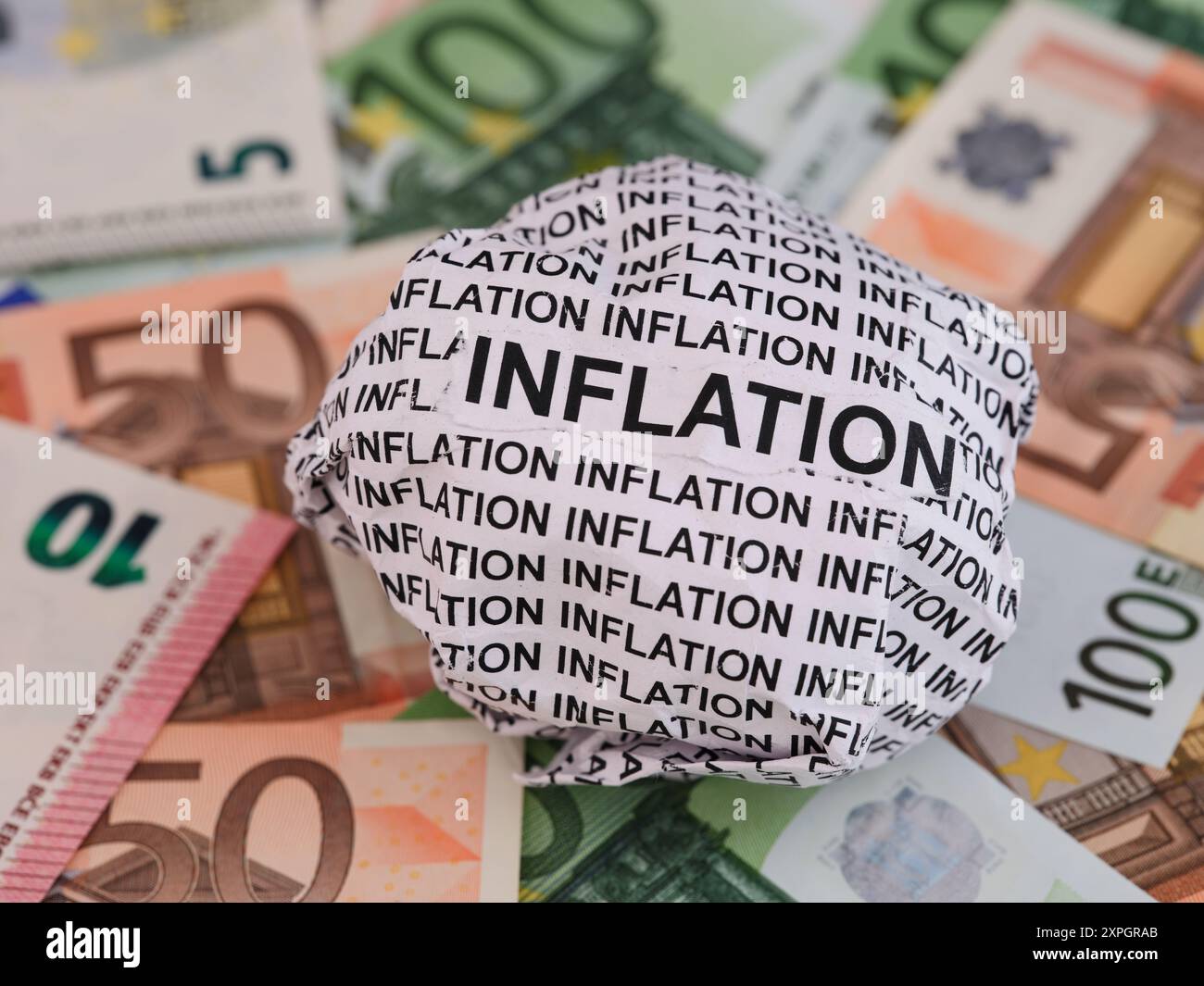 Zerknitterte Papierkugel mit Worten Inflation, die auf dem Hintergrund der Euro-Rechnungen liegen. Stockfoto