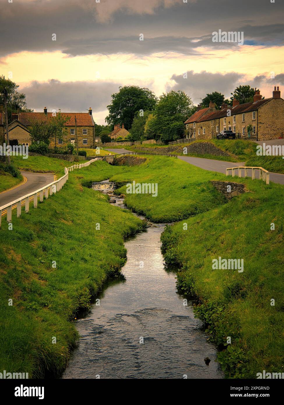 Blick entlang des Bands in Hutton le Hole, einem bezaubernden, wunderschönen Dorf in North Yorkshire mit goldenem Post-Sturmlicht, das das Wasser taucht Stockfoto
