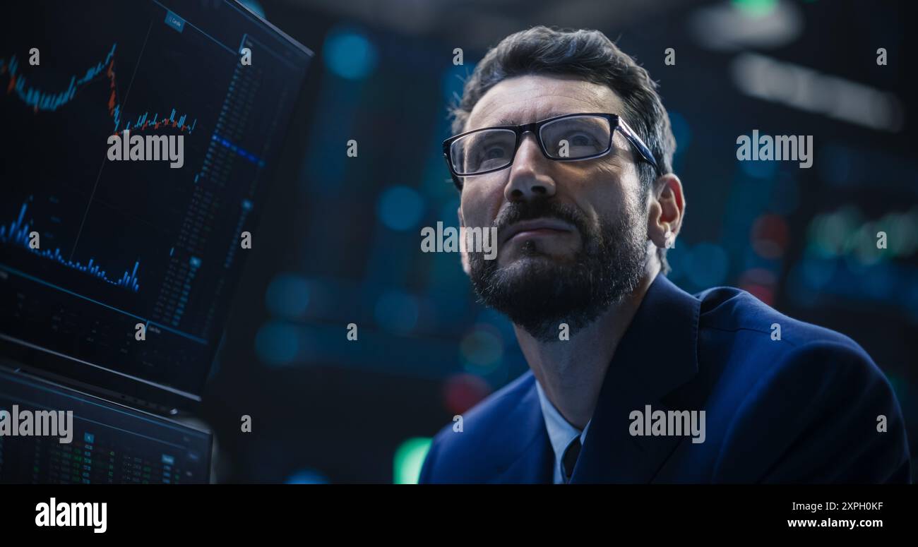 Porträt eines gutaussehenden bärtigen Börsenhändlers, der in einer Börse arbeitet. Erwachsener Mann mit Brille, erforscht Investitionsmöglichkeiten für internationale Unternehmen Stockfoto
