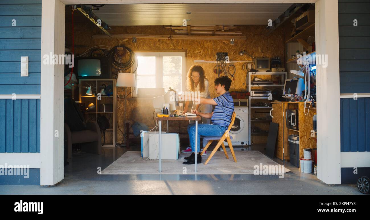 Kaukasischer männlicher Software-Entwickler und hispanischer weiblicher Designer sprechen und verwenden alten Desktop-Computer in der Retro-Garage. Verschiedene Startup-Gründer, Die In Den 90Er Jahren Am Online Service Arbeiten. Nostalgiekonzept Stockfoto