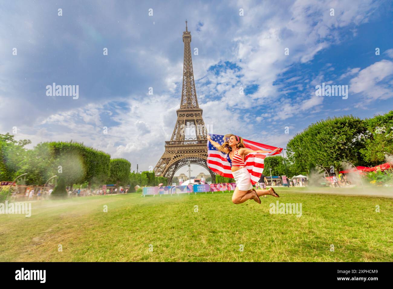 Patriotische Amerikanerin springt und jubelt für das Team USA und die Olympischen Spiele 2024 in Paris vor dem Eiffelturm, Paris, Frankreich, Europa Stockfoto