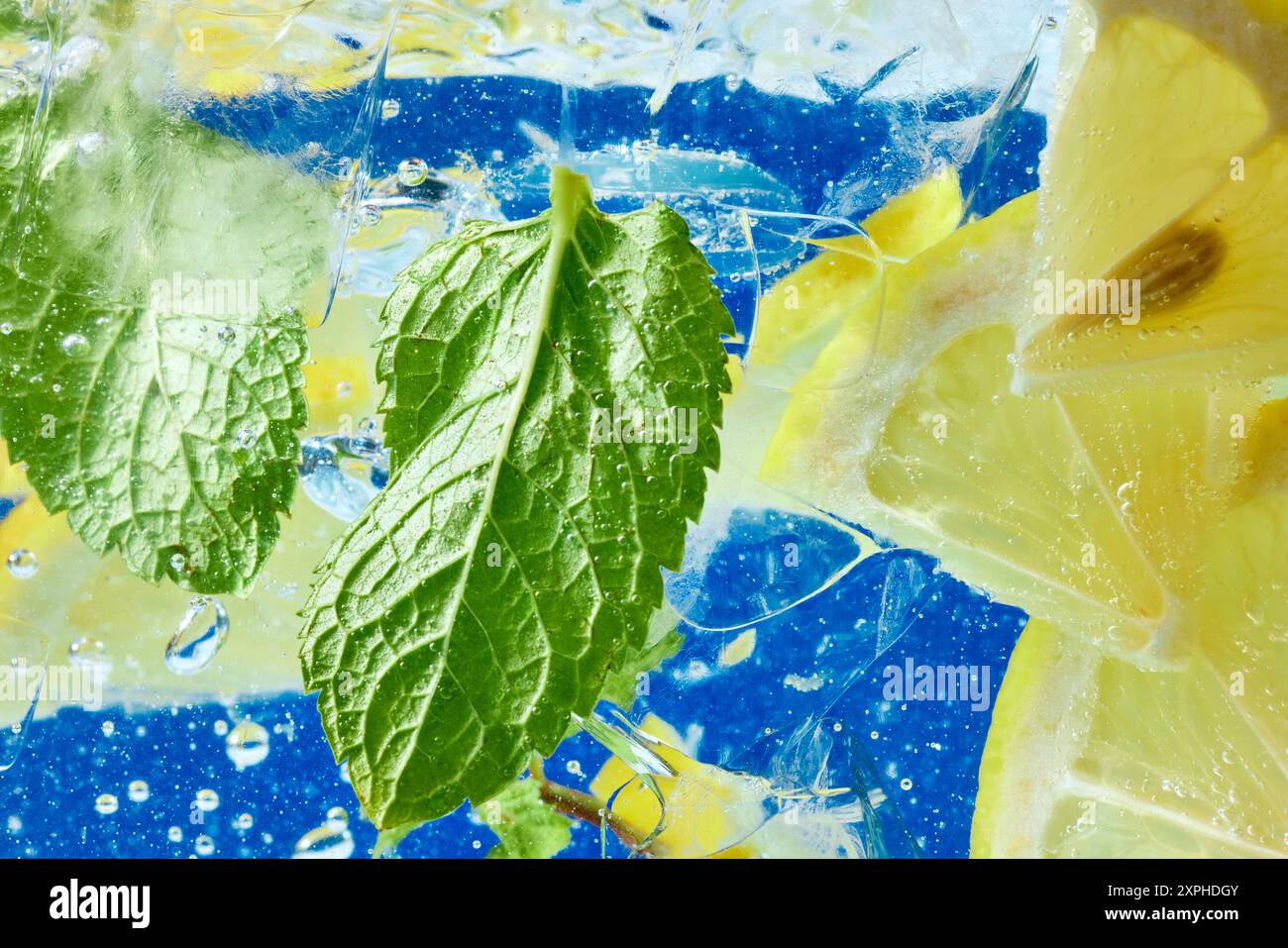Frische Zitronenscheiben und Minzblätter schwimmen in sprudelndem Wasser vor blauem Hintergrund. Strukturierte Tapete. Stockfoto