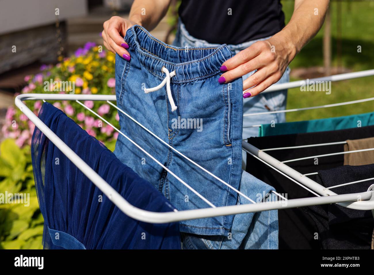 Die Frau hängt draußen die Wäsche auf einem Kleiderständer im Garten auf. Hausarbeiten Stockfoto