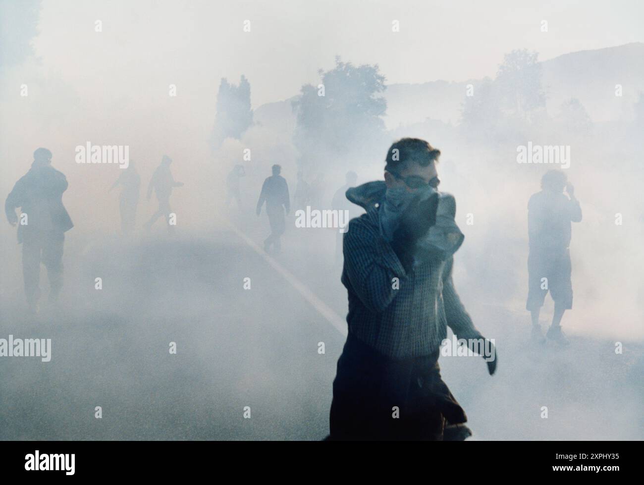 Bild von Menschen, die ihre Gesichter bedecken und während eines Protestes durch eine dicke Wolke aus Tränengas gehen. Stockfoto