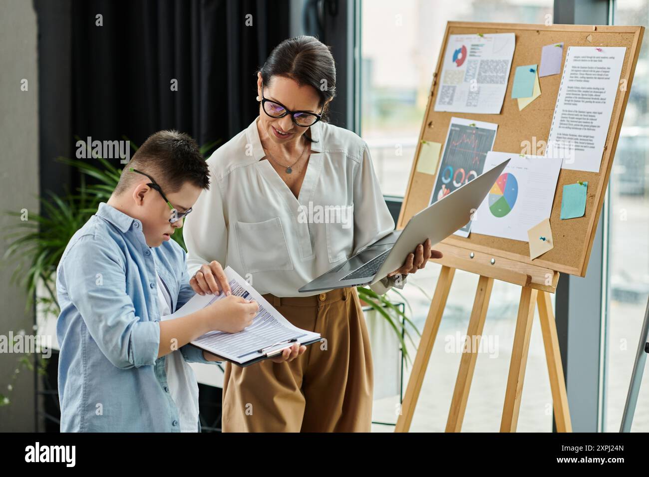 Eine Mutter und ihr Sohn mit Down-Syndrom arbeiten in einem Büro zusammen und zeigen Inklusion und Vielfalt. Stockfoto