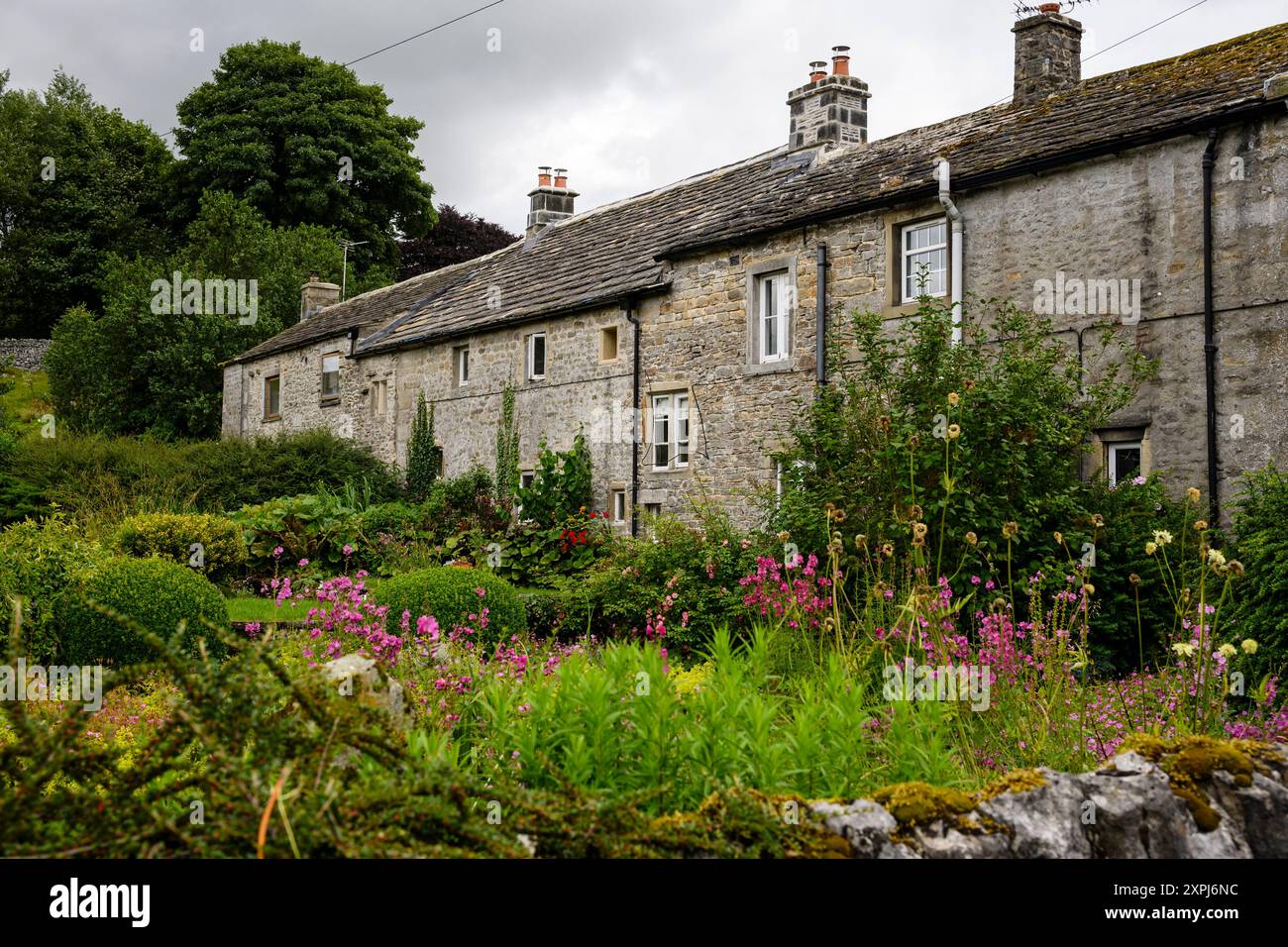 Grassington Yorkshire Großbritannien - 27. Juli 2024. Bezaubernde Steinhäuser, umgeben von üppigen Gärten und lebhaften Blumen an einem bewölkten Tag. Stockfoto