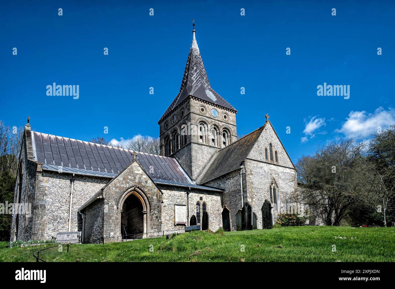 All Saints Kirche in East Meon, Hampshire, vor einem hellblauen Himmel, der von der Straße aufblickt Stockfoto