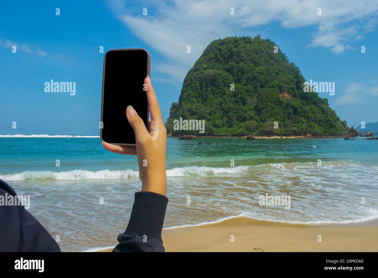 Smartphone-Mockup am Meeresstrand, Nahaufnahme einer weiblichen Hand, die ein Mobiltelefon mit leerem schwarzen Bildschirm als Kopierraum an der Küste im Sommer hält, se Stockfoto