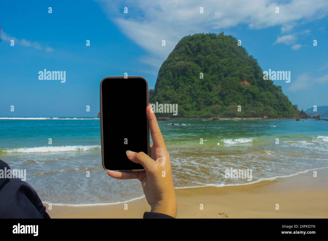 Smartphone-Mockup am Meeresstrand, Nahaufnahme einer weiblichen Hand, die ein Mobiltelefon mit leerem schwarzen Bildschirm als Kopierraum an der Küste im Sommer hält, se Stockfoto