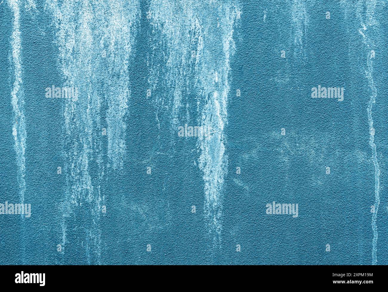Blaue, grungy strukturierte Wand mit weißen Flecken, die in einem abstrakten Landschaftsbild nach unten verlaufen. Stockfoto