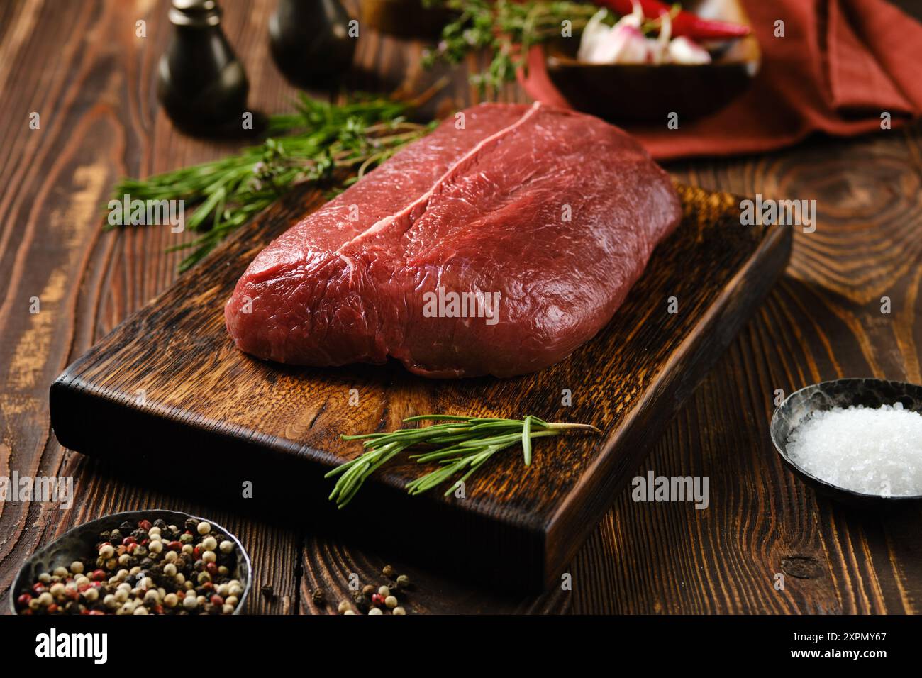 Rohes Rindersteak mit oberer Klinge auf hölzernem Schneidebrett, umgeben von Gewürzen und Kräutern Stockfoto