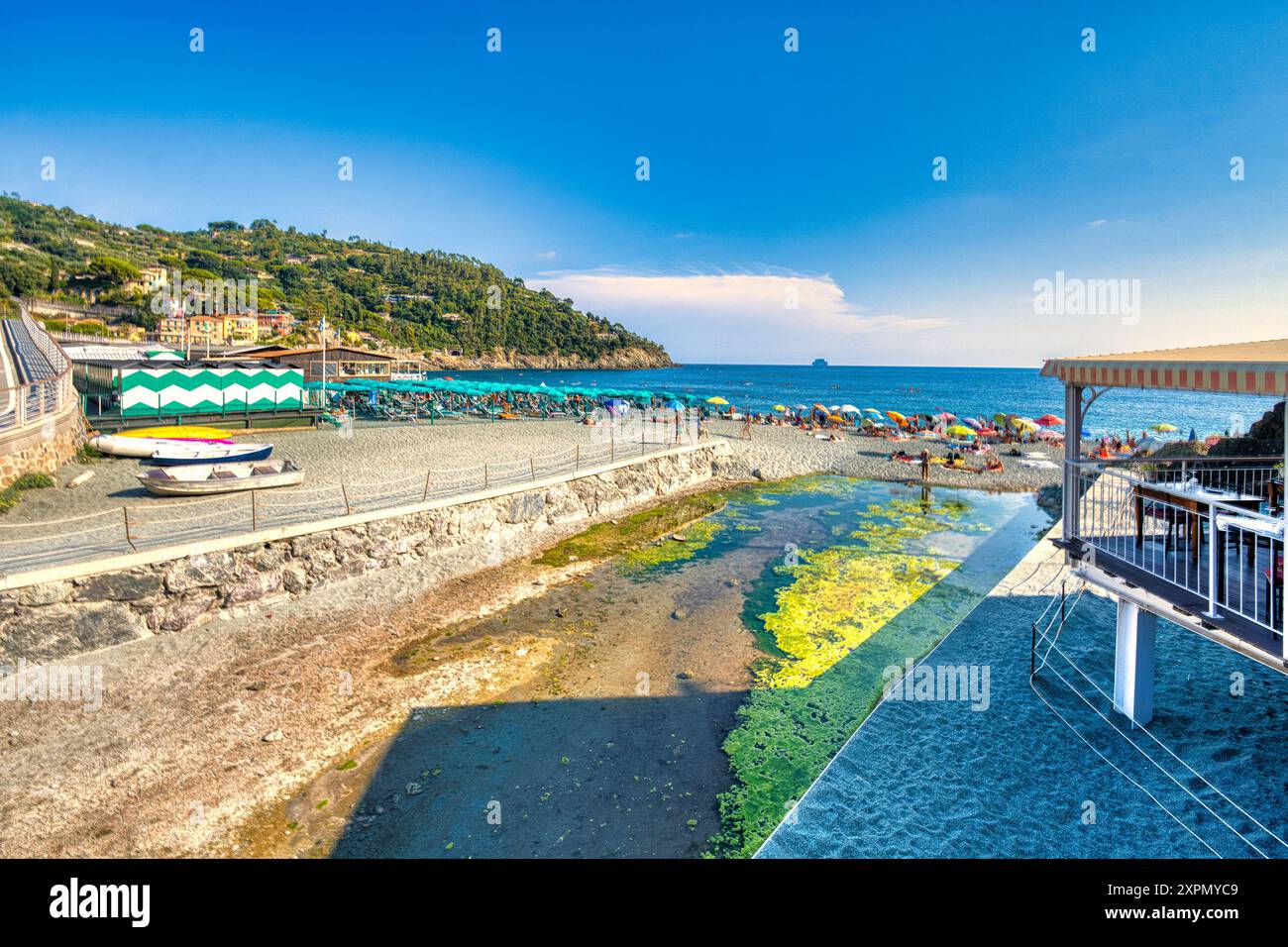 Ein lebhafter Strand mit bunten Sonnenschirmen, ruhigem Meer und einer charmanten Stadt am Hügel im Hintergrund. Perfekt für einen Sommerurlaub. Stockfoto