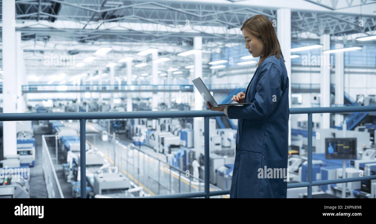 Porträt eines schönen japanischen Ingenieurs, der einen Laptop benutzt und sich in einer Fabrik umsieht, in der Geräte zur Herstellung moderner elektronischer Bauteile für verschiedene Branchen hergestellt werden Stockfoto