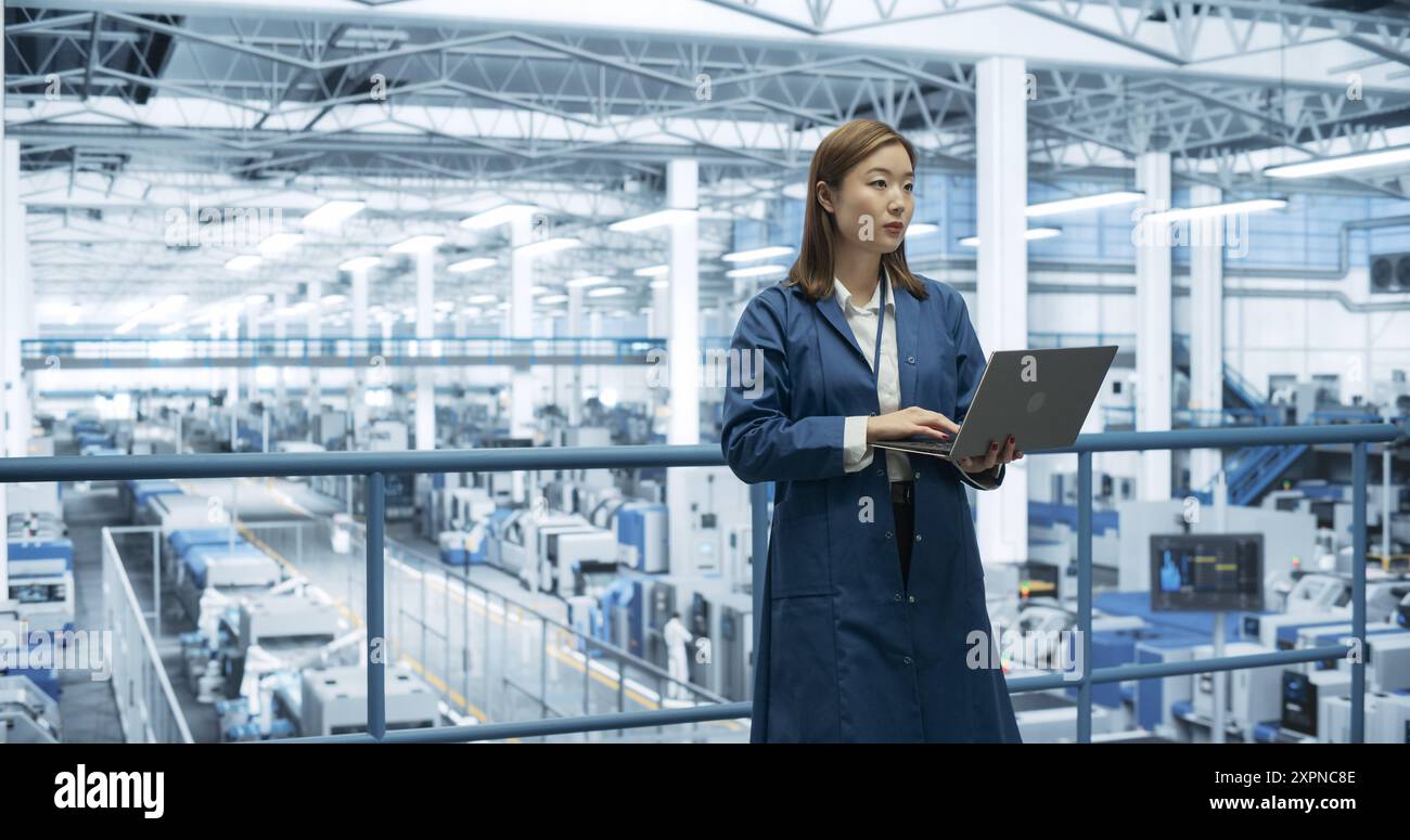 Porträt eines schönen japanischen Ingenieurs, der einen Laptop benutzt und sich in einer Fabrik umsieht, in der Geräte zur Herstellung moderner elektronischer Bauteile für verschiedene Branchen hergestellt werden Stockfoto