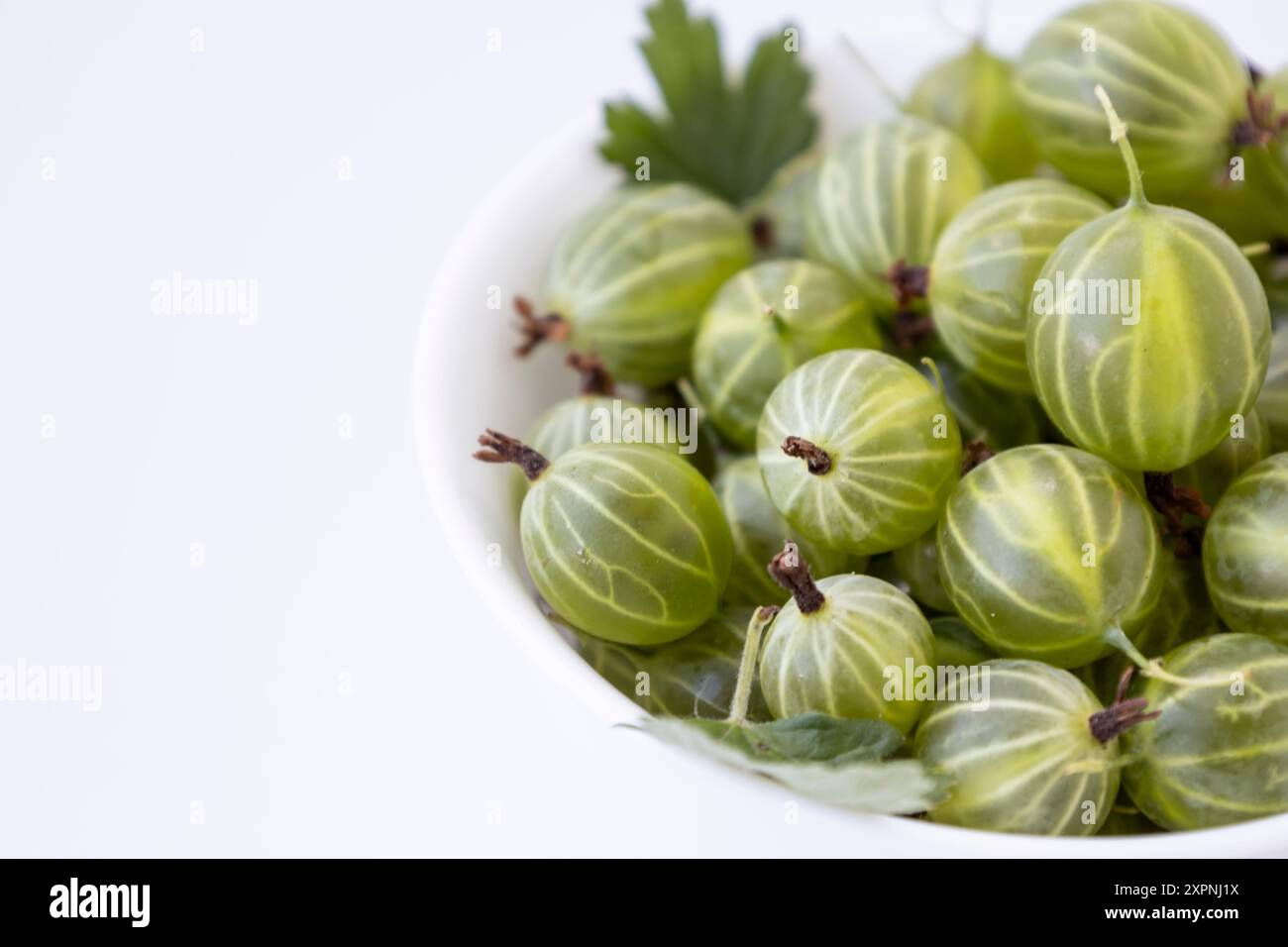 Stachelbeerfrucht mit Blattfedern auf der weißen Platte auf weißem Hintergrund. Saftige frische, reife grüne Bio-Beeren Stachelbeere Stockfoto