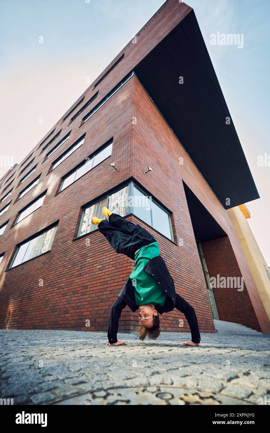 Der Tänzer trotzt der Schwerkraft mit einem umgedrehten Handstand, leuchtend gelben Schuhen, die in den Himmel zeigen und von urbaner Architektur eingerahmt werden. Stockfoto