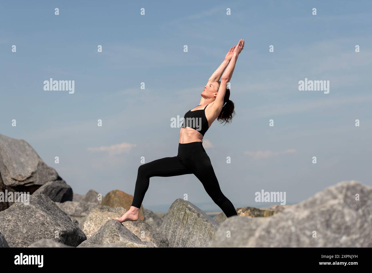 Frau, die eine Yoga-Ausfallposition macht, draußen mit felsigem Hintergrund Stockfoto