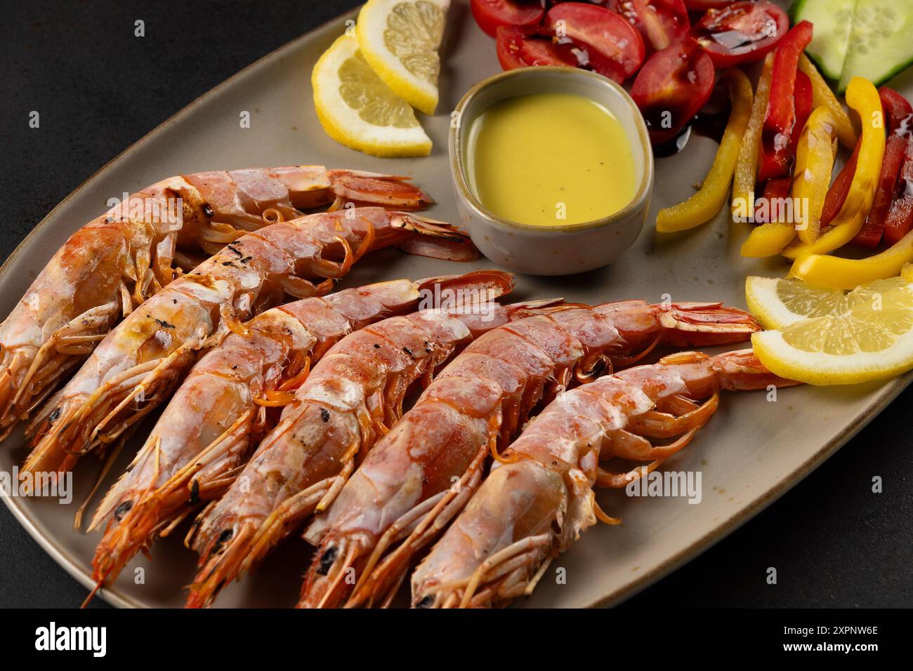 Gegrillte Garnelen auf Teller mit Zitronenscheibe und Gemüse. Meeresfrüchte im Hintergrund. Stockfoto