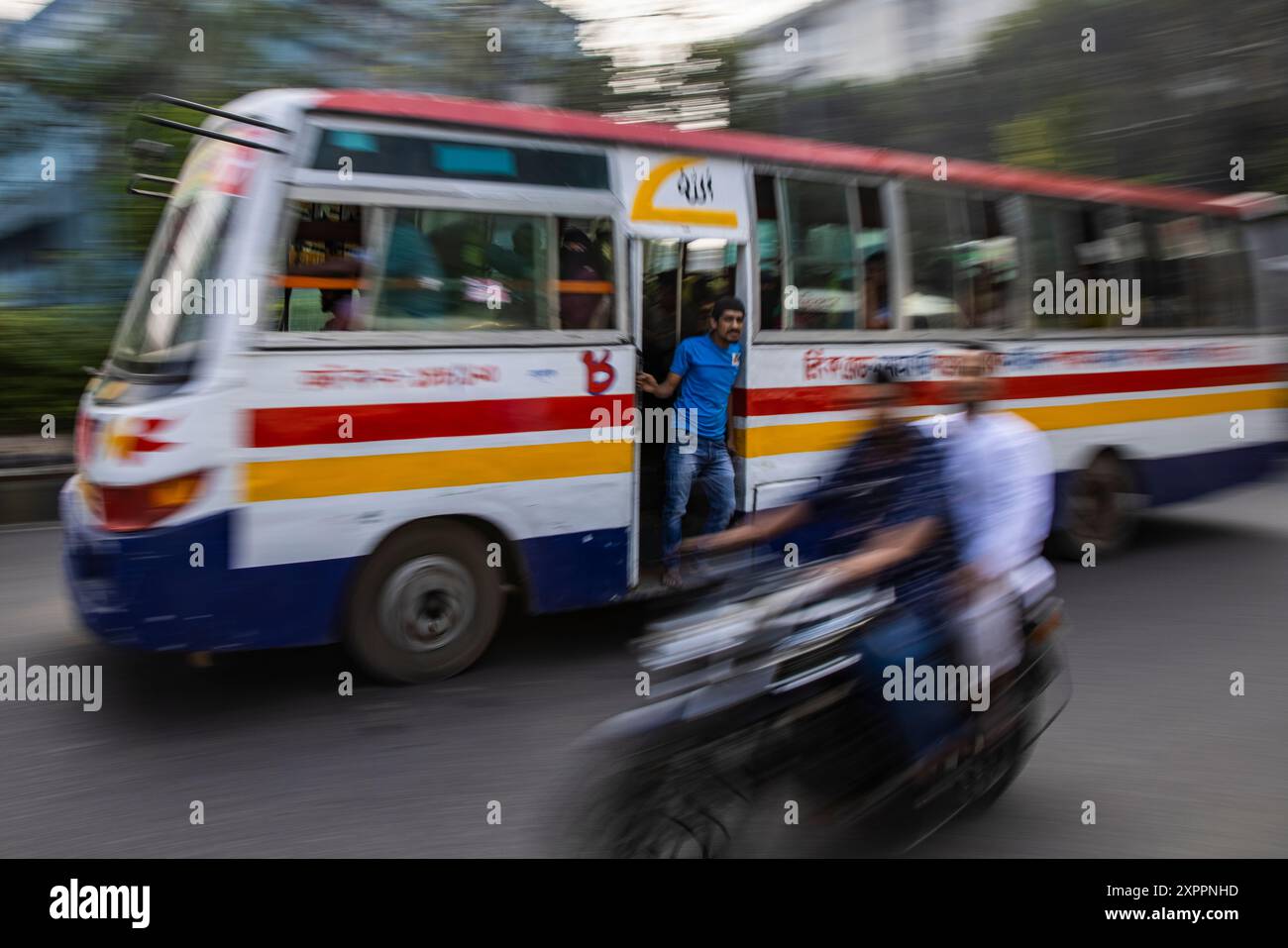 Zoomtes Bild eines öffentlichen Busses mit einem Motorrad, das in der Innenstadt von Dhaka, Dhaka, Bangladesch, Asien vorbeifährt Stockfoto