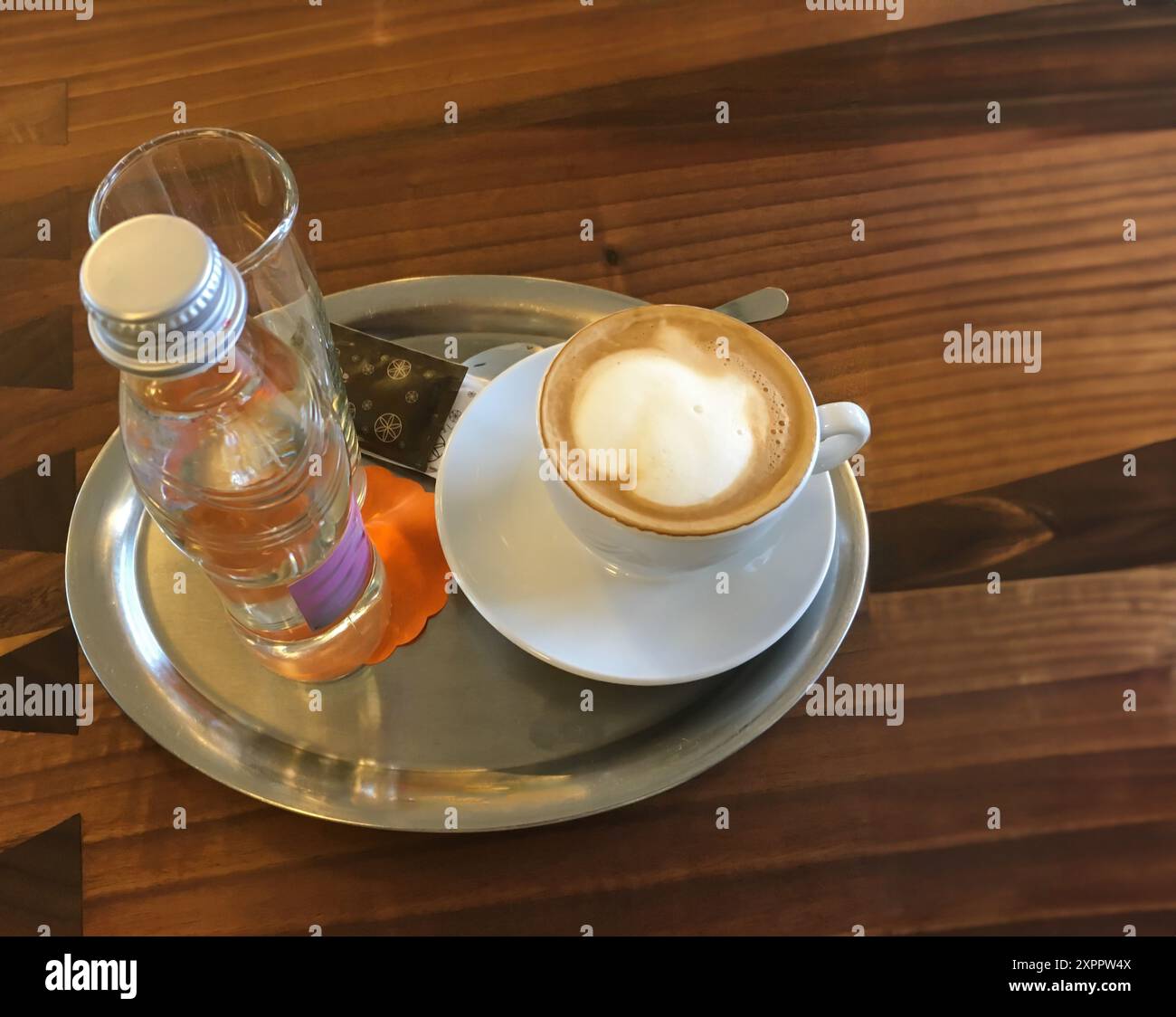 Cappuccino und Mineralwasser auf einem verzierten Holztisch in Slowenien Stockfoto